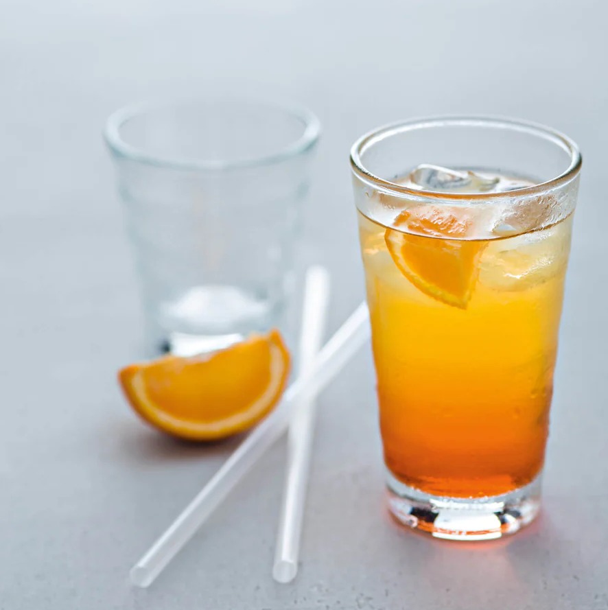 Zwei Gläser  eines leer mit Orangenscheibe  eines mit orangefarbenem Getränk und Eis  schräg freigestellt fotografiert