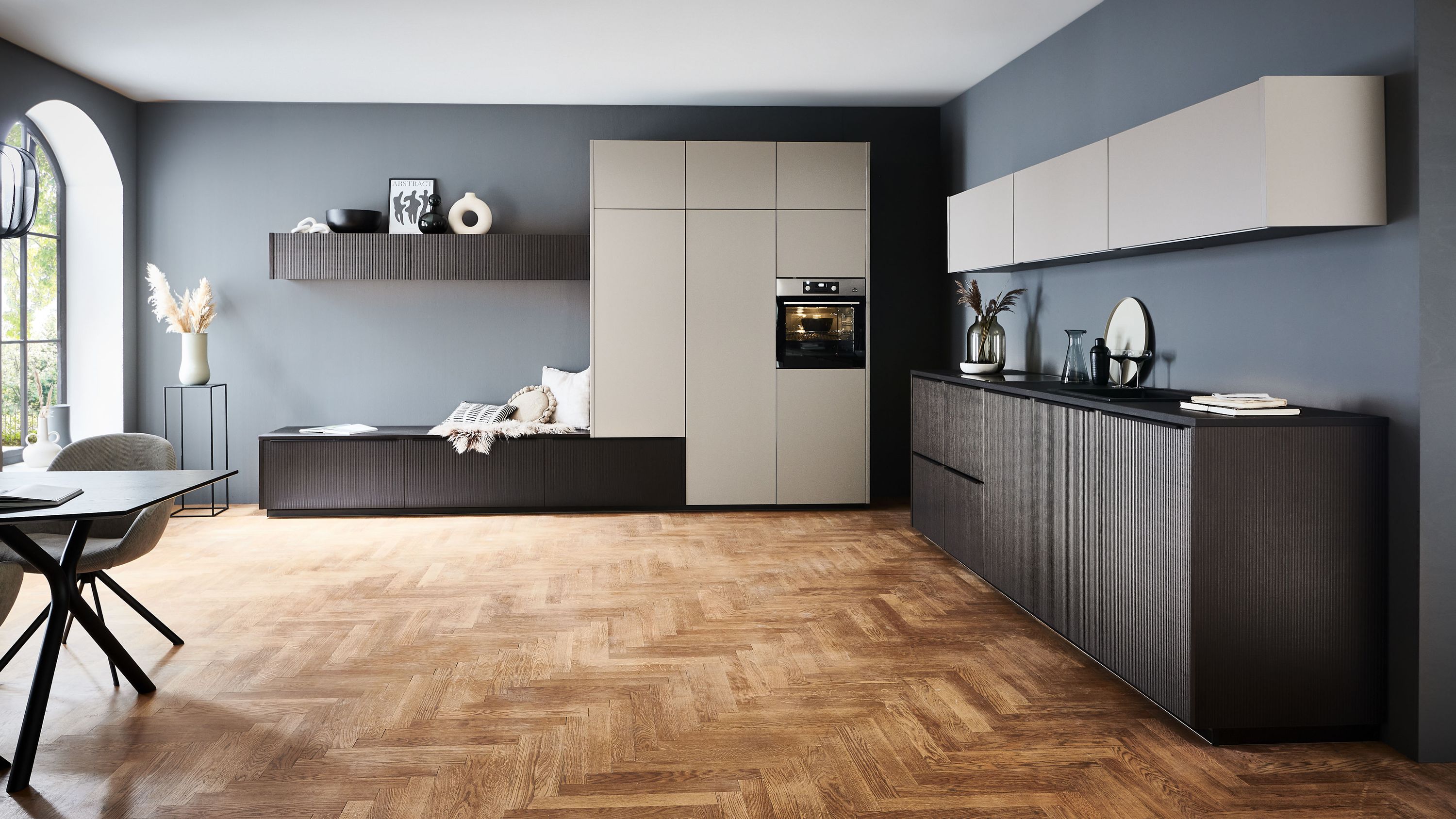 Minimalistische Küche mit Kontrastfronten und Fischgrätboden Küche mit dunklen Unterschränken grauen Oberschränken Fischgrätboden Bogenfenster und schwarzer Arbeitsplatte