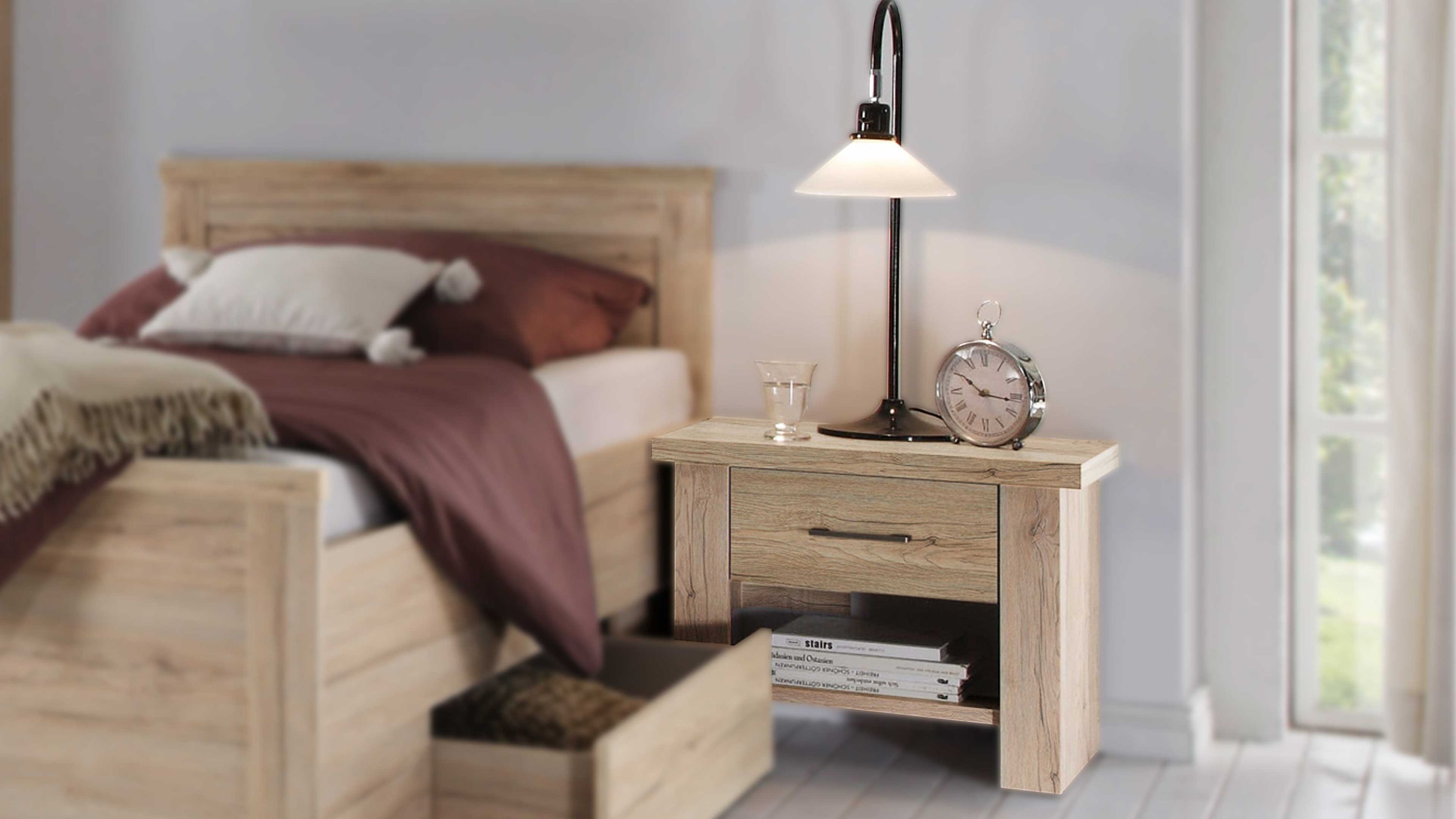 Nachtkommode mit zwei Schubladen in heller Holzoptik neben einem Bett mit brauner Bettwäsche
