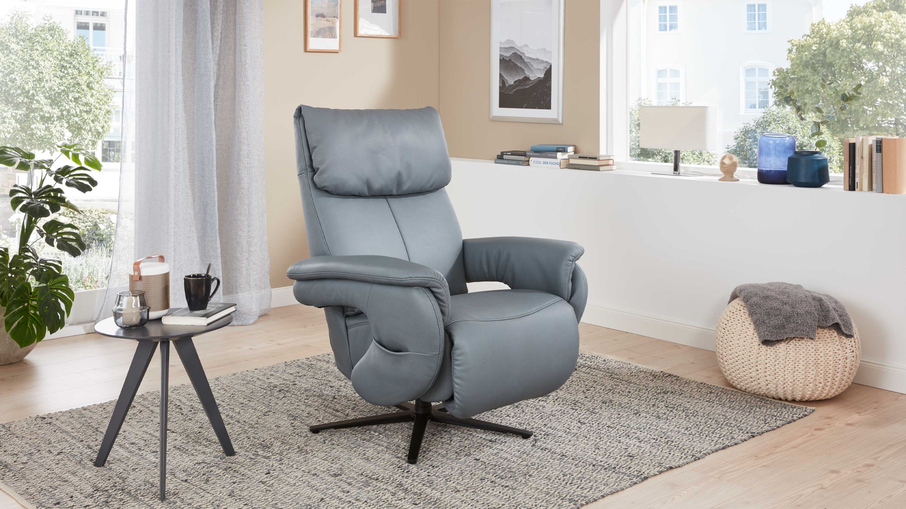 Blauer Relaxsessel mit Sternfuß Blauer Relaxsessel mit gepolsterten Armlehnen und anthrazitfarbenem Sternfuß in hellem Wohnzimmer