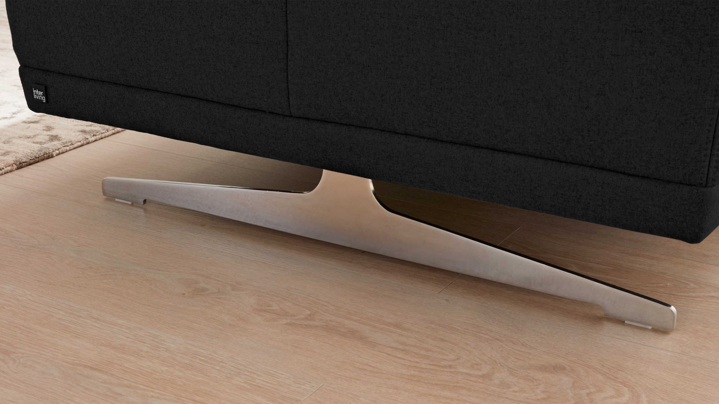 Sofa mit schwarzem Stoffbezug und verchromtem Metallfuß in V-Form auf hellem Holzboden