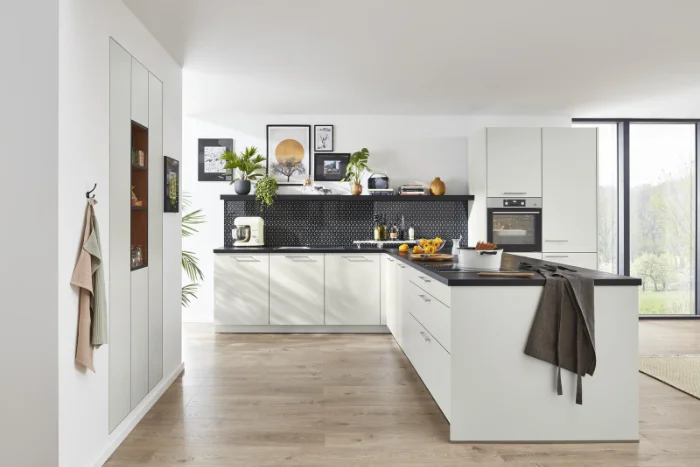 Moderne offene Küche in Weiß mit Kücheninsel, schwarzen Arbeitsplatten und Rückwand in Wabenoptik, vor bodentiefer Fensterfront.