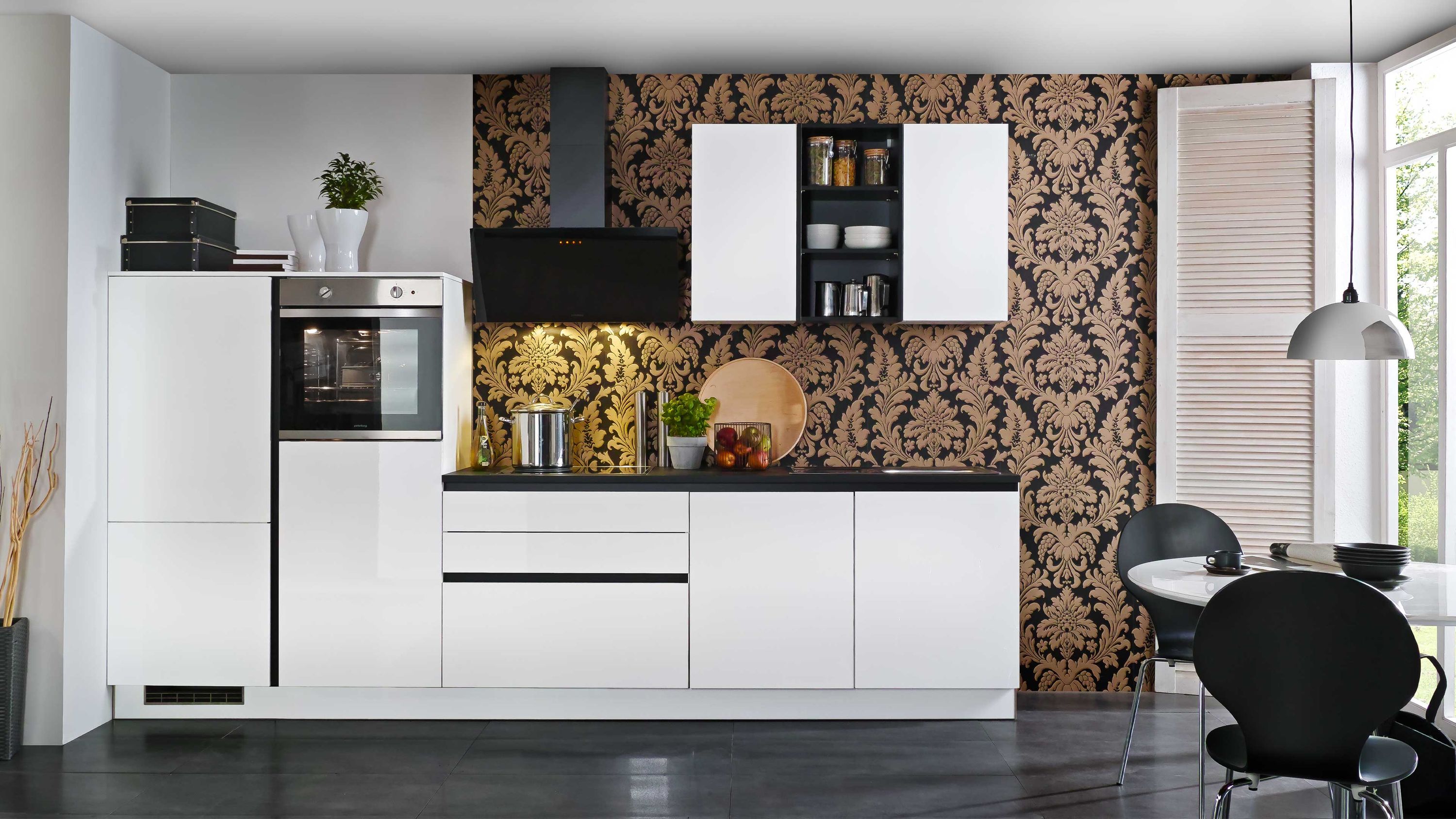Elegante Weiß-Schwarz-Küche mit luxuriösem Wanddesign. Moderne weiße Küchenzeile mit schwarzer Arbeitsplatte vor auffälliger gold-schwarzer Musterwand.