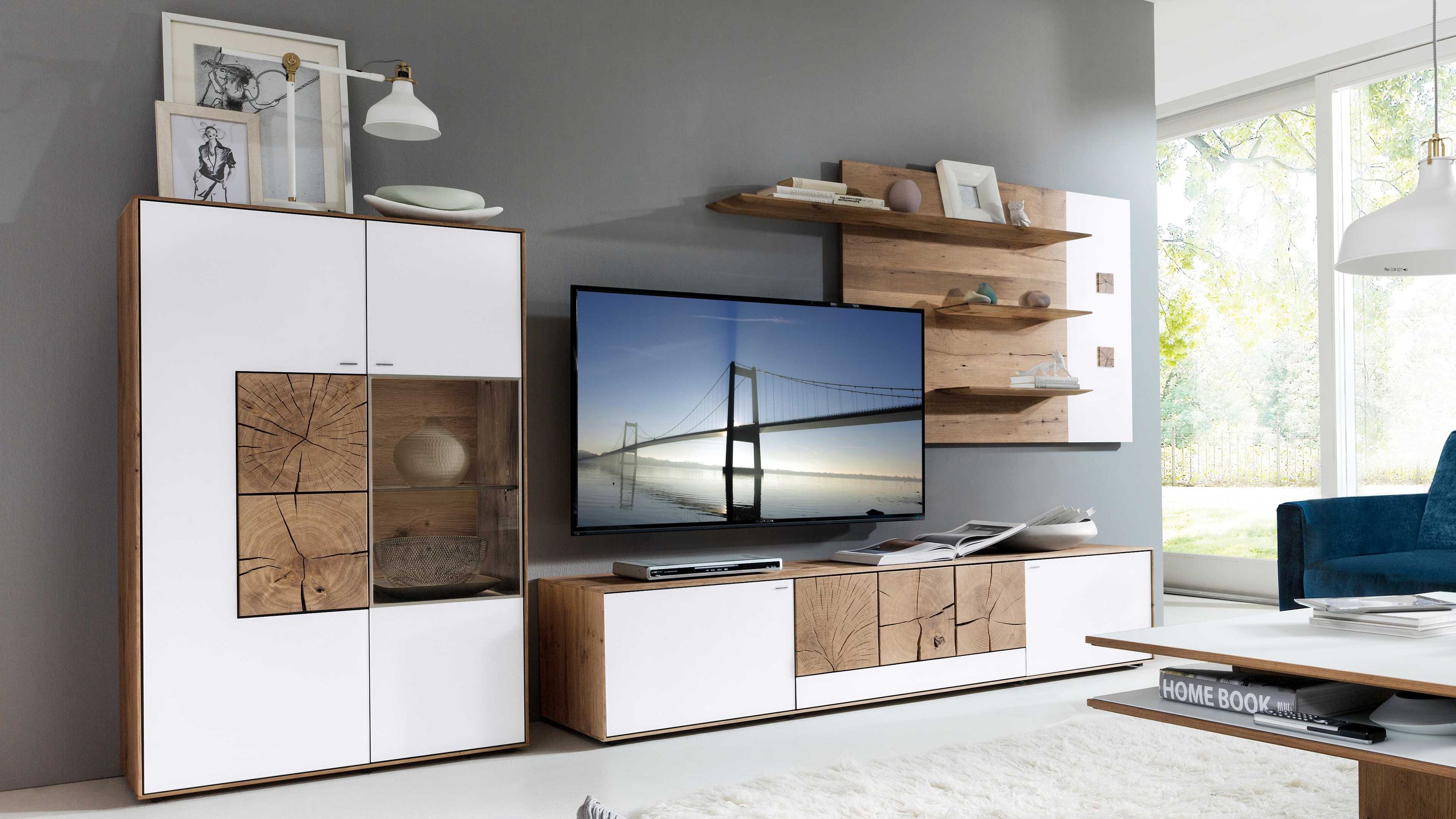 Wohnwand mit Vitrinenschrank und Regalen in Weiß und Holzoptik Wohnwand mit weißen Fronten Holzdetails und Glastür bestehend aus Vitrinenschrank Regalen und TV-Board