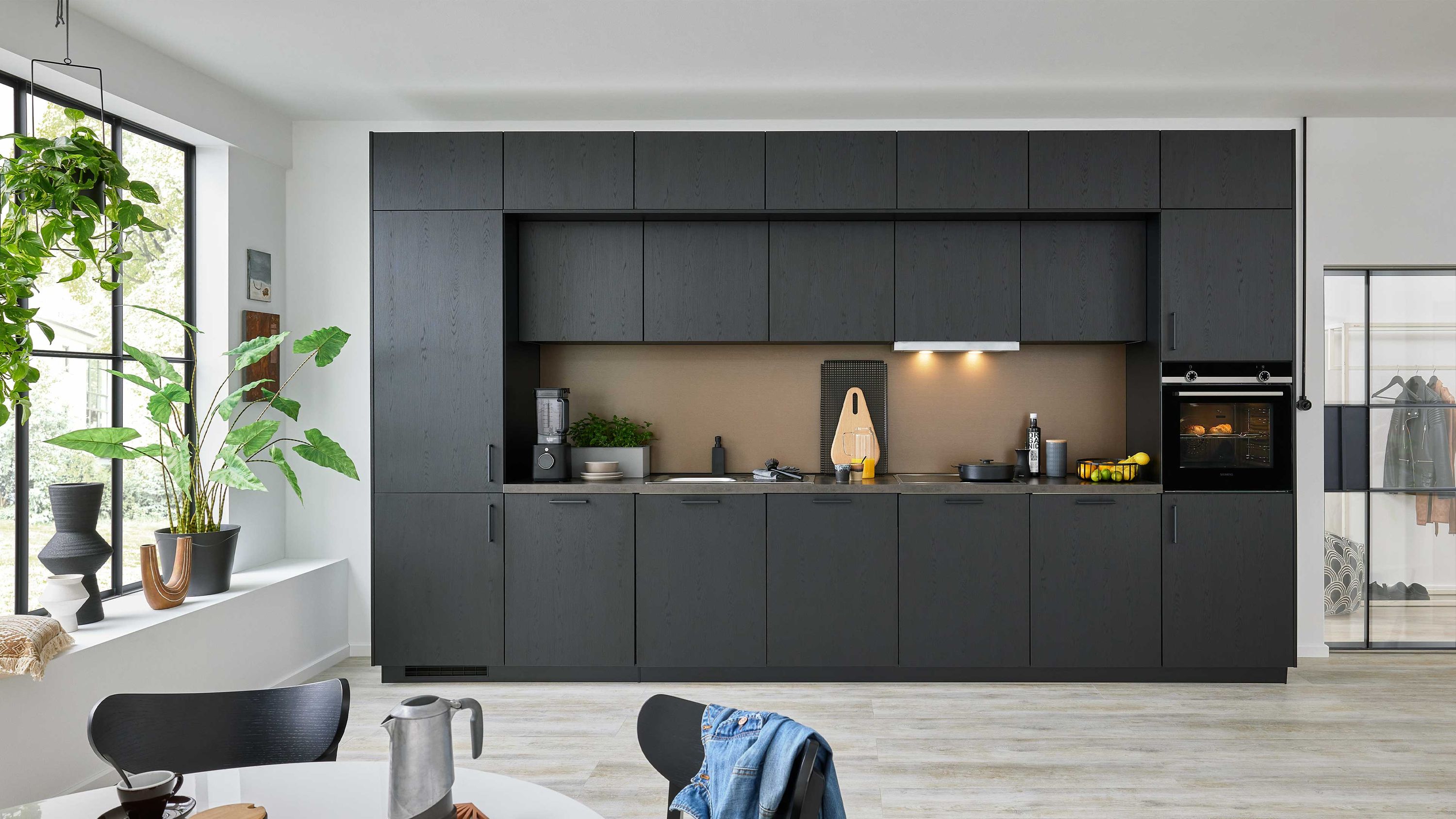 Dunkle Küche mit Fensterdeko und Essbereich Dunkle Schränke Einbauofen helle Holzoptik; Fenster mit Pflanzen Esstisch im Vordergrund moderne Raumgestaltung