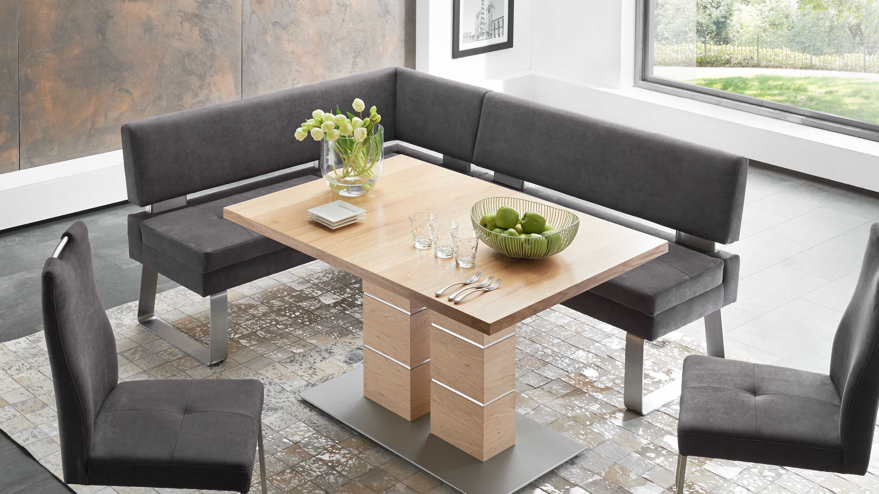 Eckbank mit anthrazitfarbener Polsterung und Metallbeinen dazu zwei Stühle und ein rechteckiger Holztisch mit Metallfuß