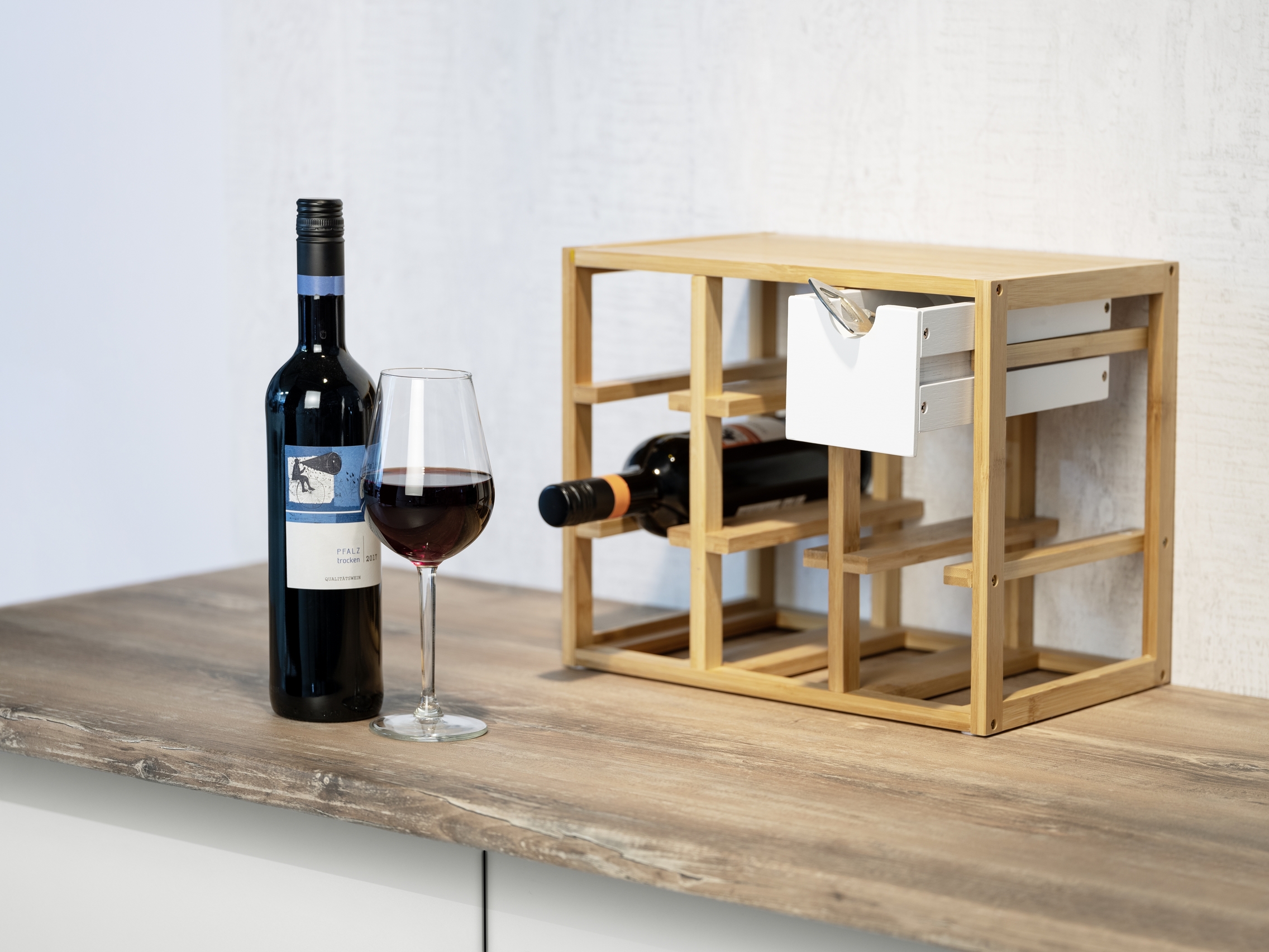 Weinregal aus braunem Bambus mit zwei Flaschen daneben Rotweinflasche und gefülltes Glas schräg von rechts aufgenommen