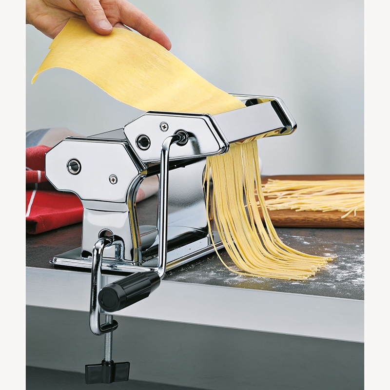 Handkurbel-Nudelmaschine mit eingespannter Teigplatte  frische Pasta kommt aus Walze  am Tisch befestigt