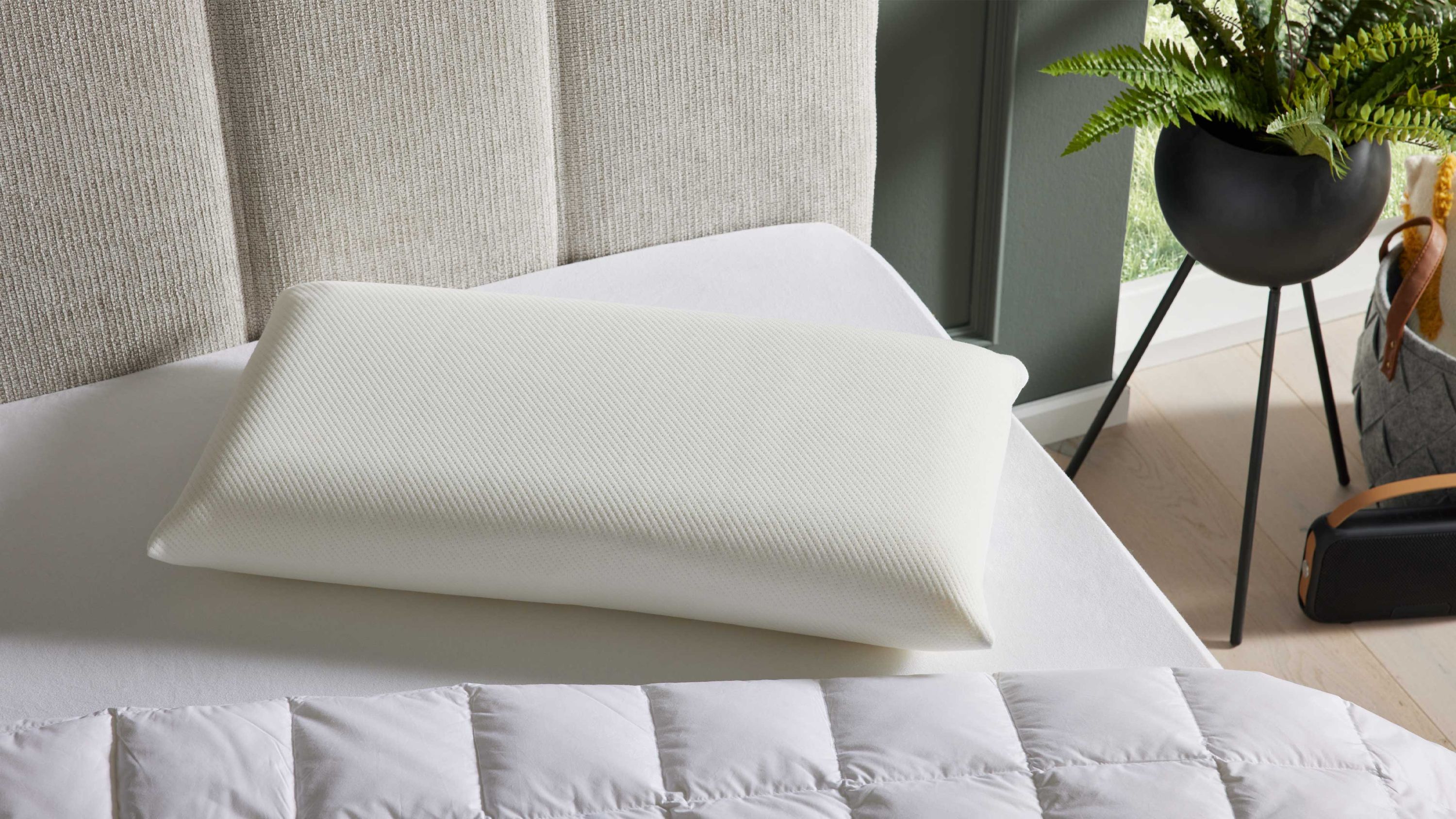 Weißes Nackenstützkissen mit ergonomischer Form auf weißem Bett mit grauem Kopfteil