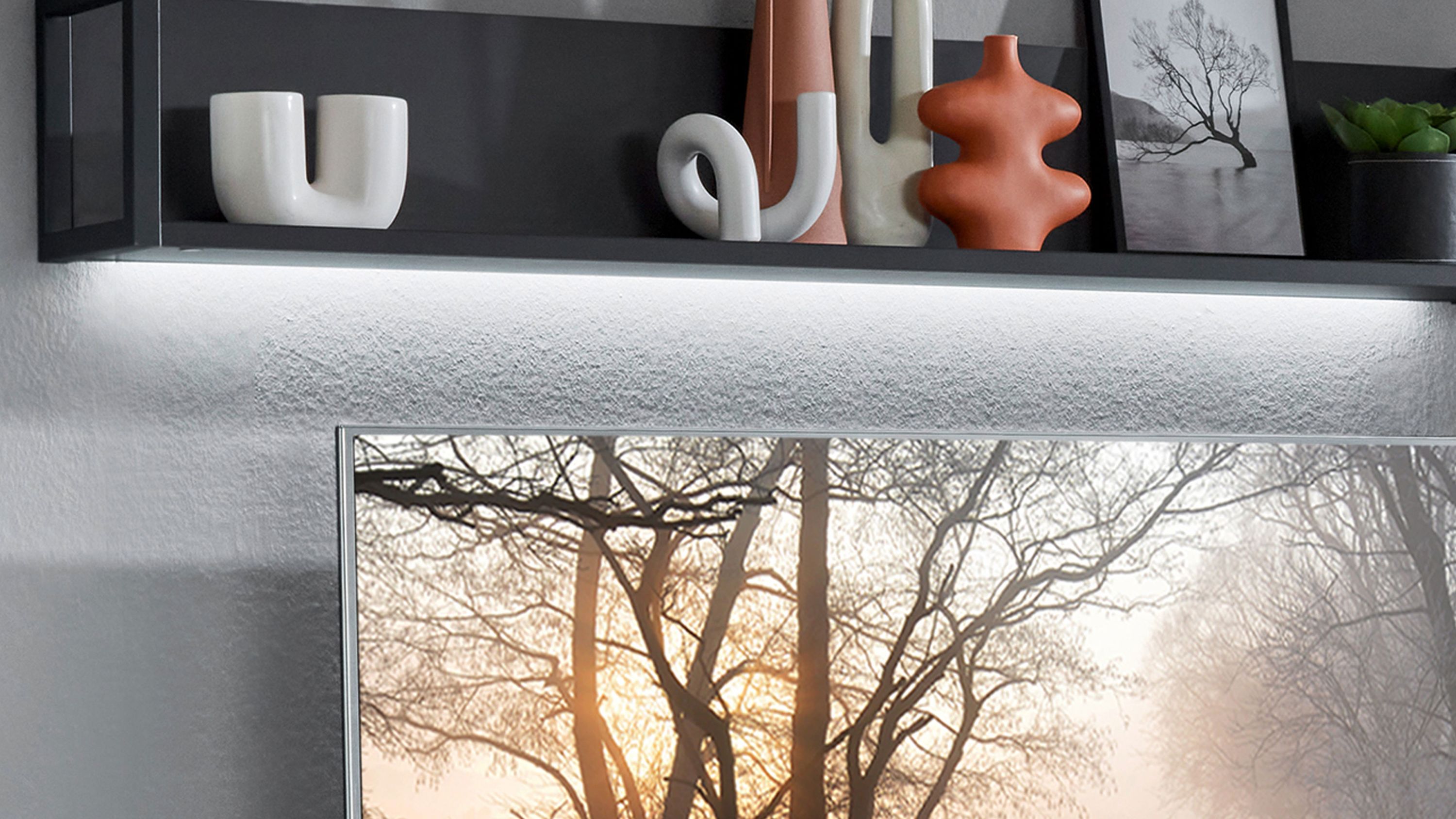 Wandregal mit LED-Beleuchtung und Dekorationsvasen Schwarzes Wandregal mit LED-Beleuchtung darunter darauf verschiedene Vasen und ein gerahmtes Bild