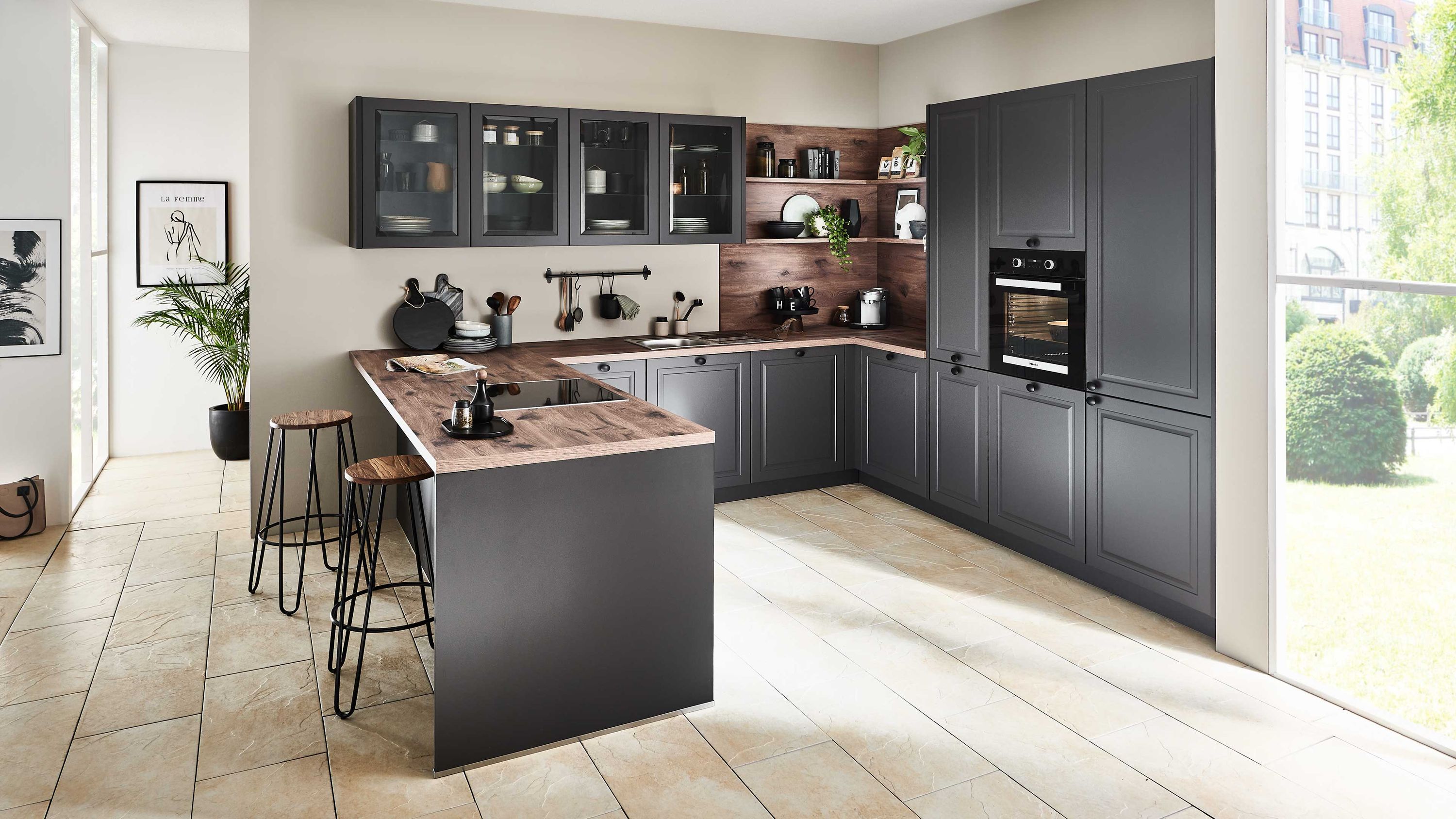 Dunkelgraue U-Küche im Landhausstil mit Holzarbeitsplatte Glashängeschränken Barbereich und Einbauofen.