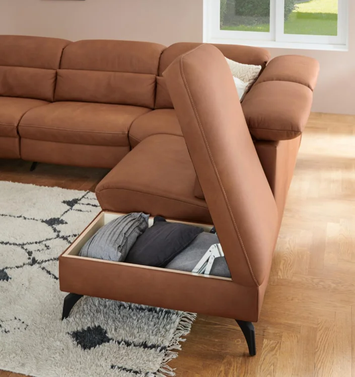 Ecksofa in Terrakotta mit aufgeklappter Sitzfläche und integriertem Stauraumfach auf Holzfußboden mit Teppich.