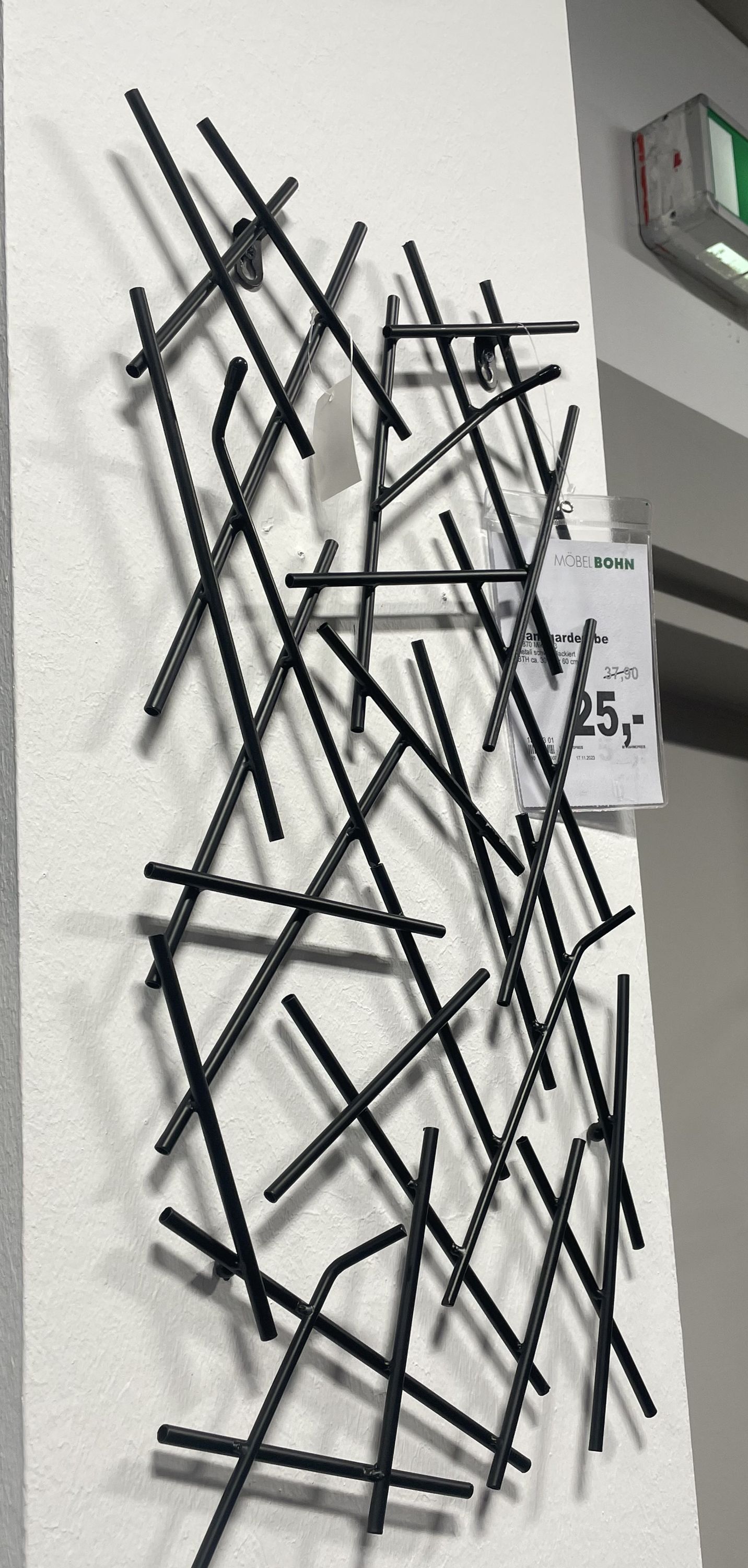 Moderne Wandgarderobe aus schwarzen Metallstäben, geometrisch angeordnet mit mehreren Haken zur Aufhängung.