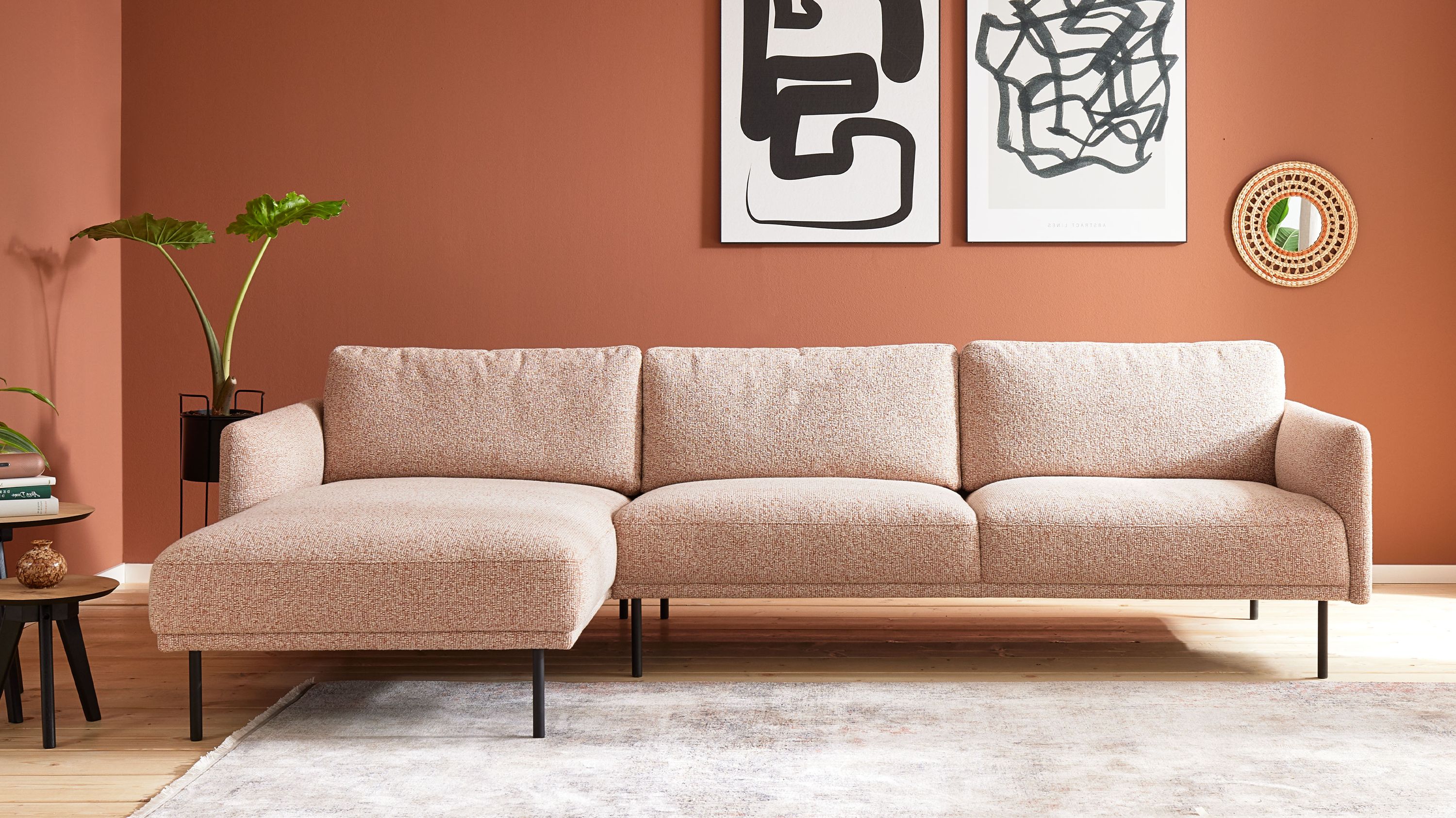 Ecksofa mit rostfarben meliertem Bezug und Metallfüßen vor rostfarbener Wand mit abstrakten Bildern