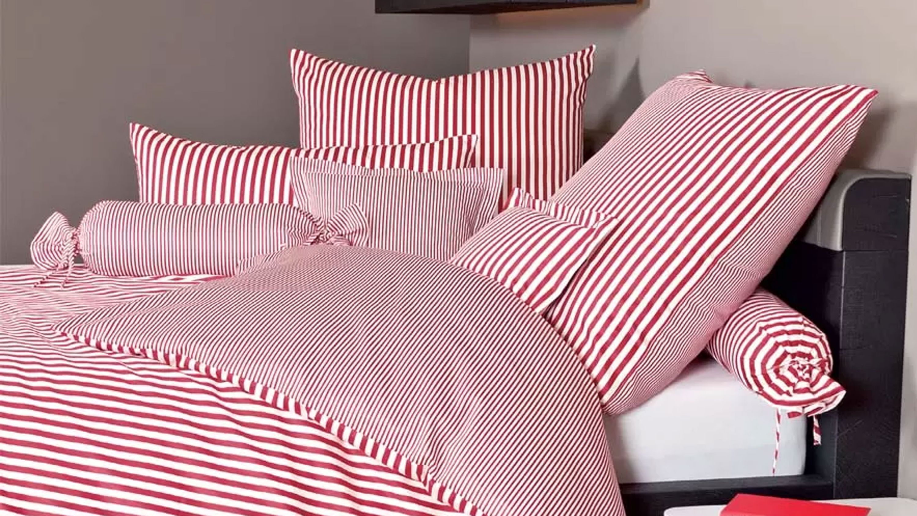 Bett mit roter und weißer gestreifter Bettwäsche und mehreren Kissen in verschiedenen Größen
