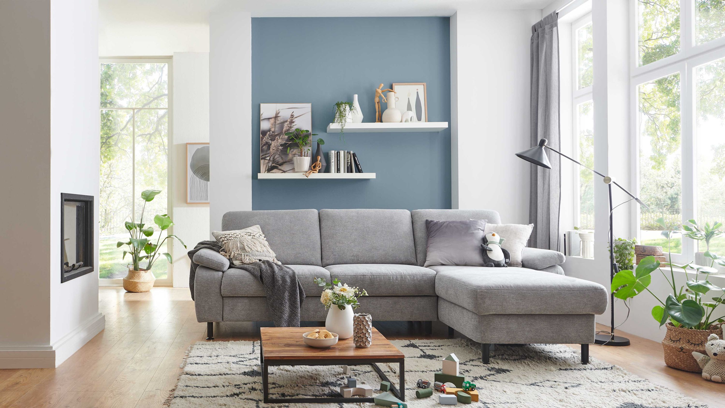 Ecksofa mit alufarbenem Stoffbezug und schwarzen Füßen in einem hellen Wohnzimmer mit Holzboden
