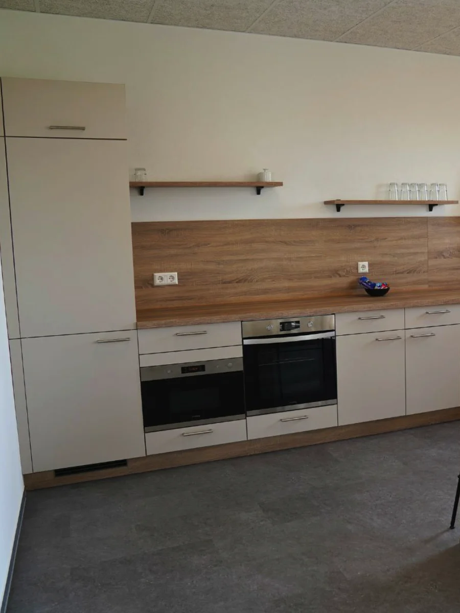 Moderne Küchenzeile mit grauen Fronten, Holzarbeitsplatte, schwarzer Spüle, Einbaugeräten, offenen Regalen und Kaffeemaschine.