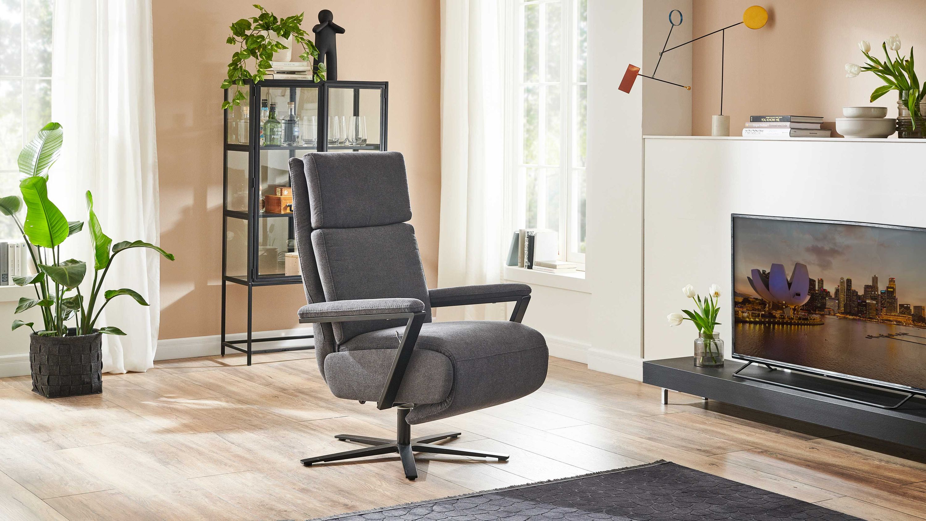 Anthrazitfarbener Relaxsessel mit schwarzem Sternfuß Anthrazitfarbener Relaxsessel mit gepolsterten Armlehnen und schwarzem Sternfuß in modernem Wohnzimmer