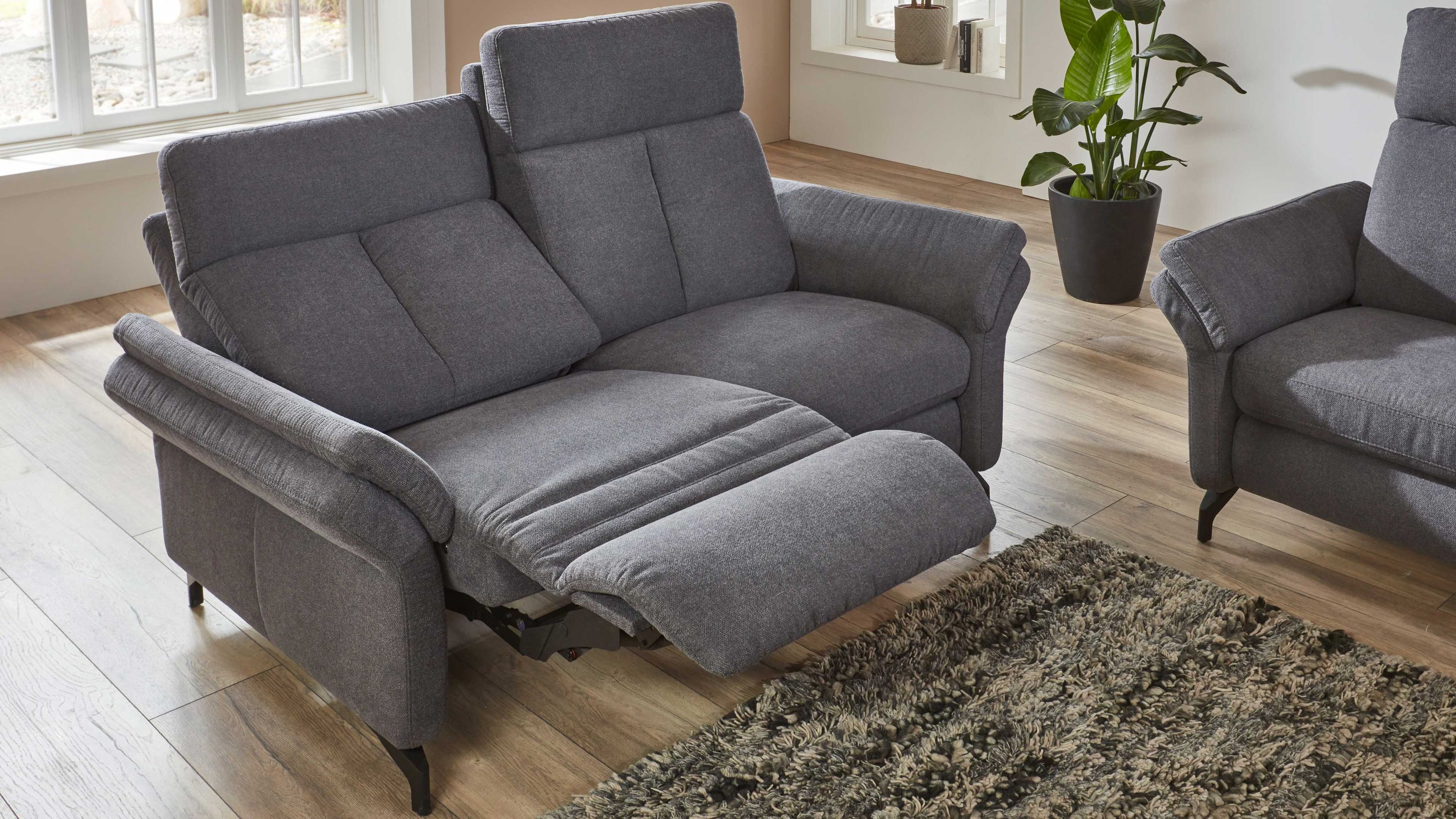 Zweisitziges Sofa mit anthrazitfarbenem Stoffbezug und ausgefahrener Fußstütze in modernem Wohnzimmer