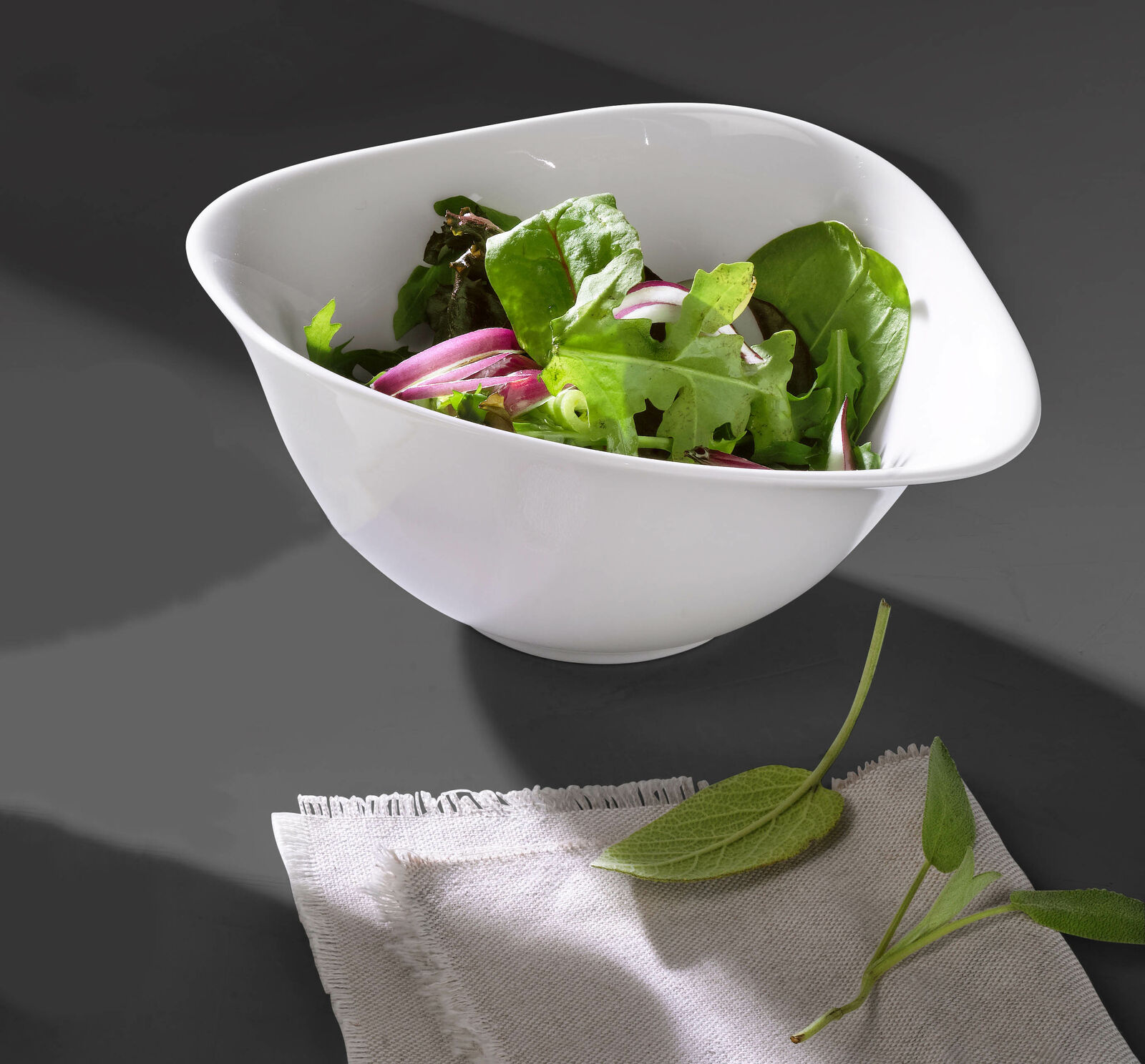 Weiße ovale Porzellanschale mit Griff aus dem Vapiano Pasta Set  gefüllt mit Salat  auf dunklem Untergrund mit Serviette