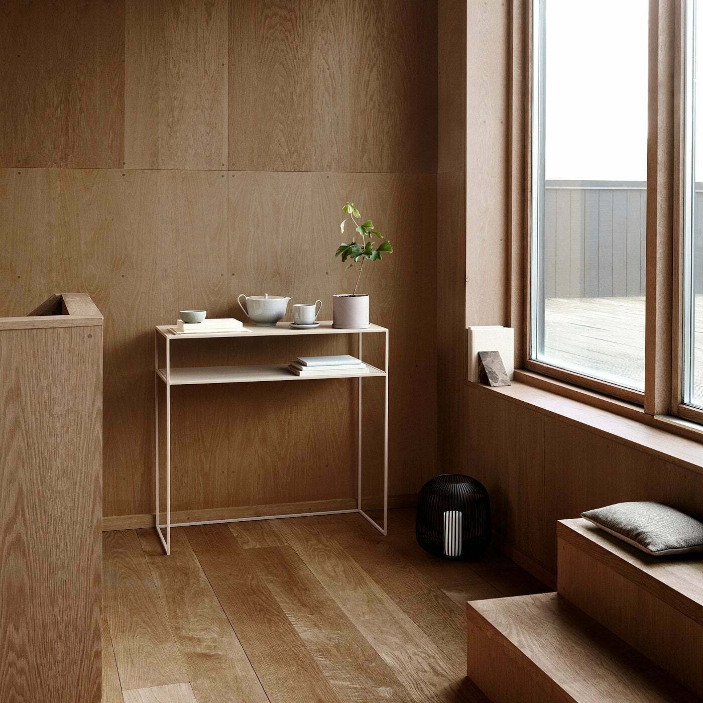 Minimalistischer Raum mit Holzverkleidung großen Fenstern und Laterne LITO aus Stahl am Fensterboden