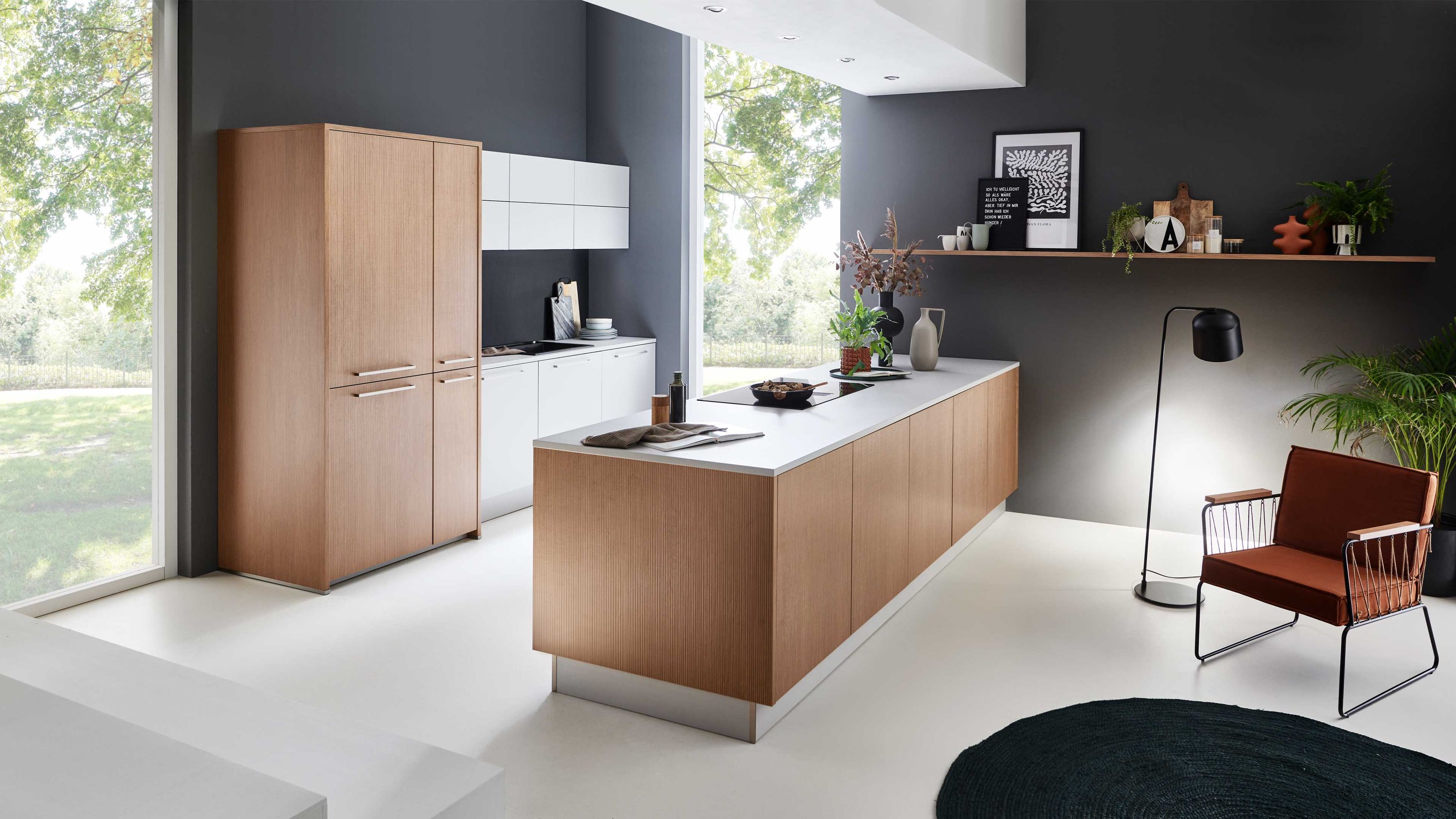 Designküche mit Holzfronten und Insel Holzschränke mit weißer Arbeitsplatte zentrale Insel Fenster links brauner Stuhl schwarze Stehlampe Tageslicht