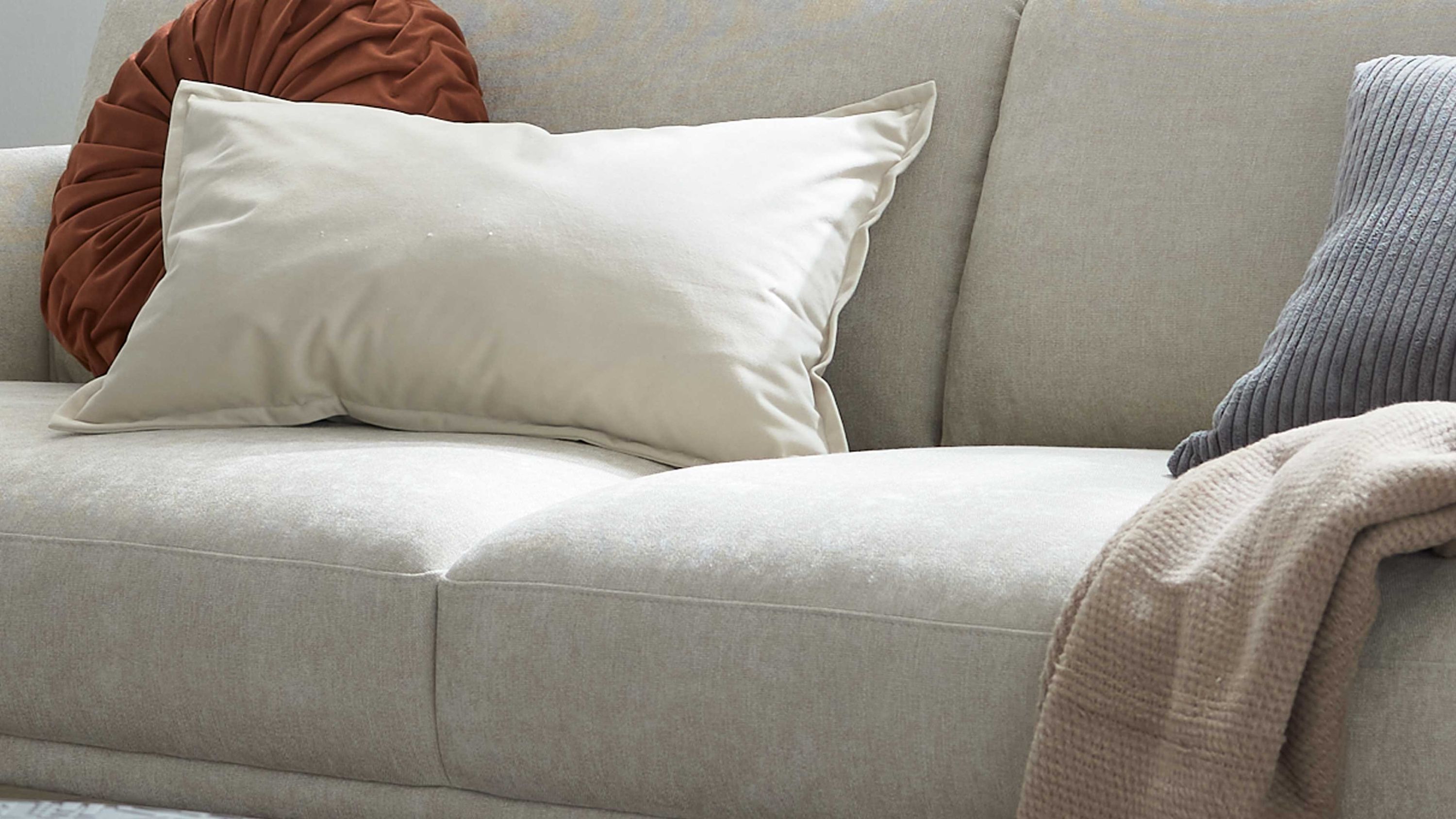 Beige rechteckige Kissenhülle auf einem hellen Sofa mit weiteren Kissen und einer Decke