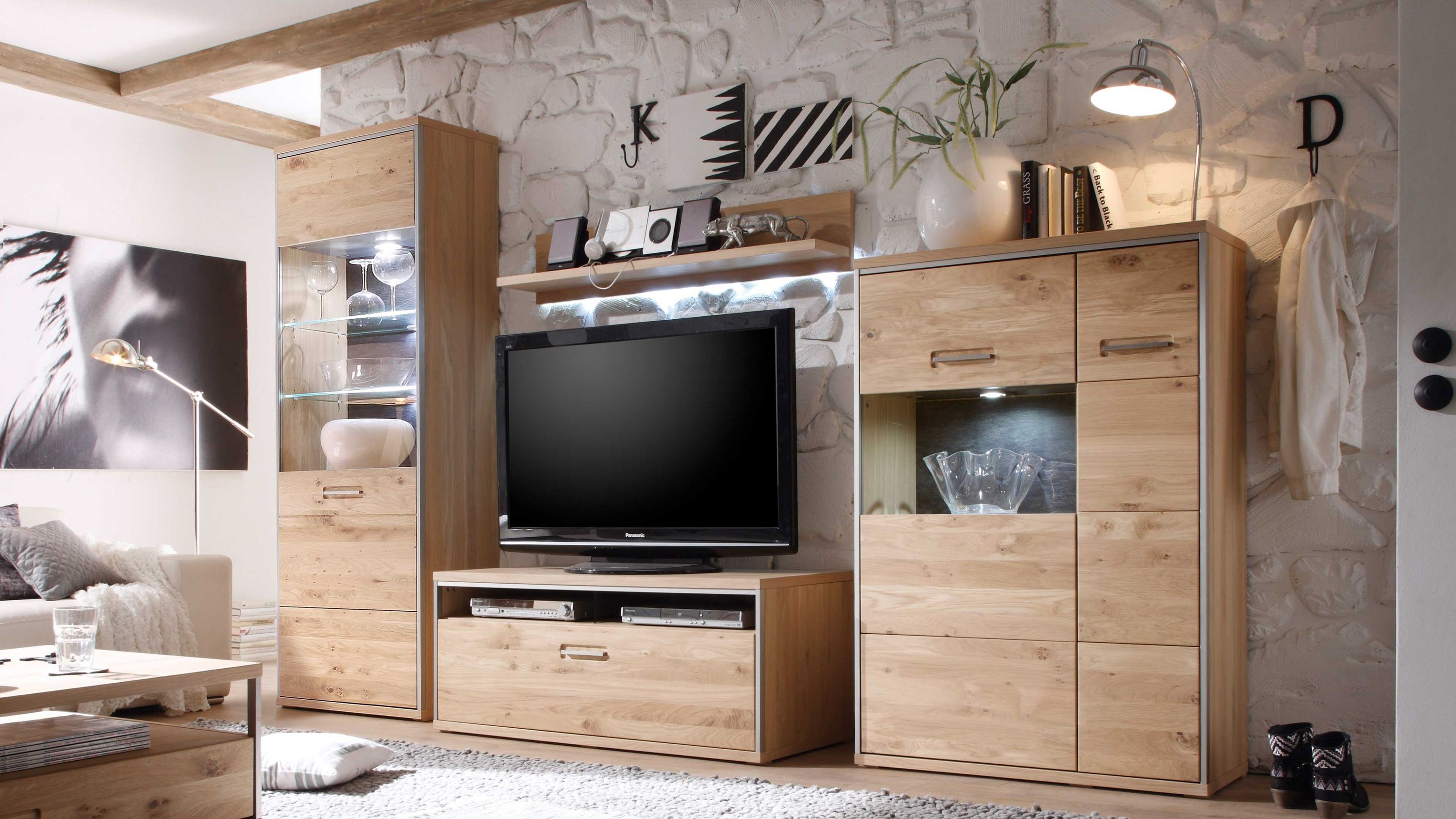 Vierteilige Wohnwand aus hellem Holz mit Vitrinenschrank TV-Board Hängeregal und Kommode vor weißer Steinwand