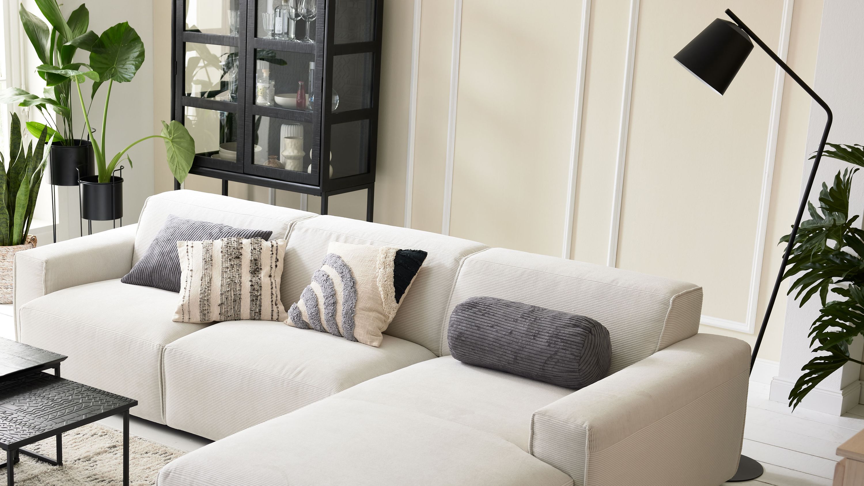 Schwarze Stehlampe aus Metall neben Sofa Stehlampe mit schwarzem Metallgestell und schrägem Lampenschirm neben weißem Sofa mit Kissen