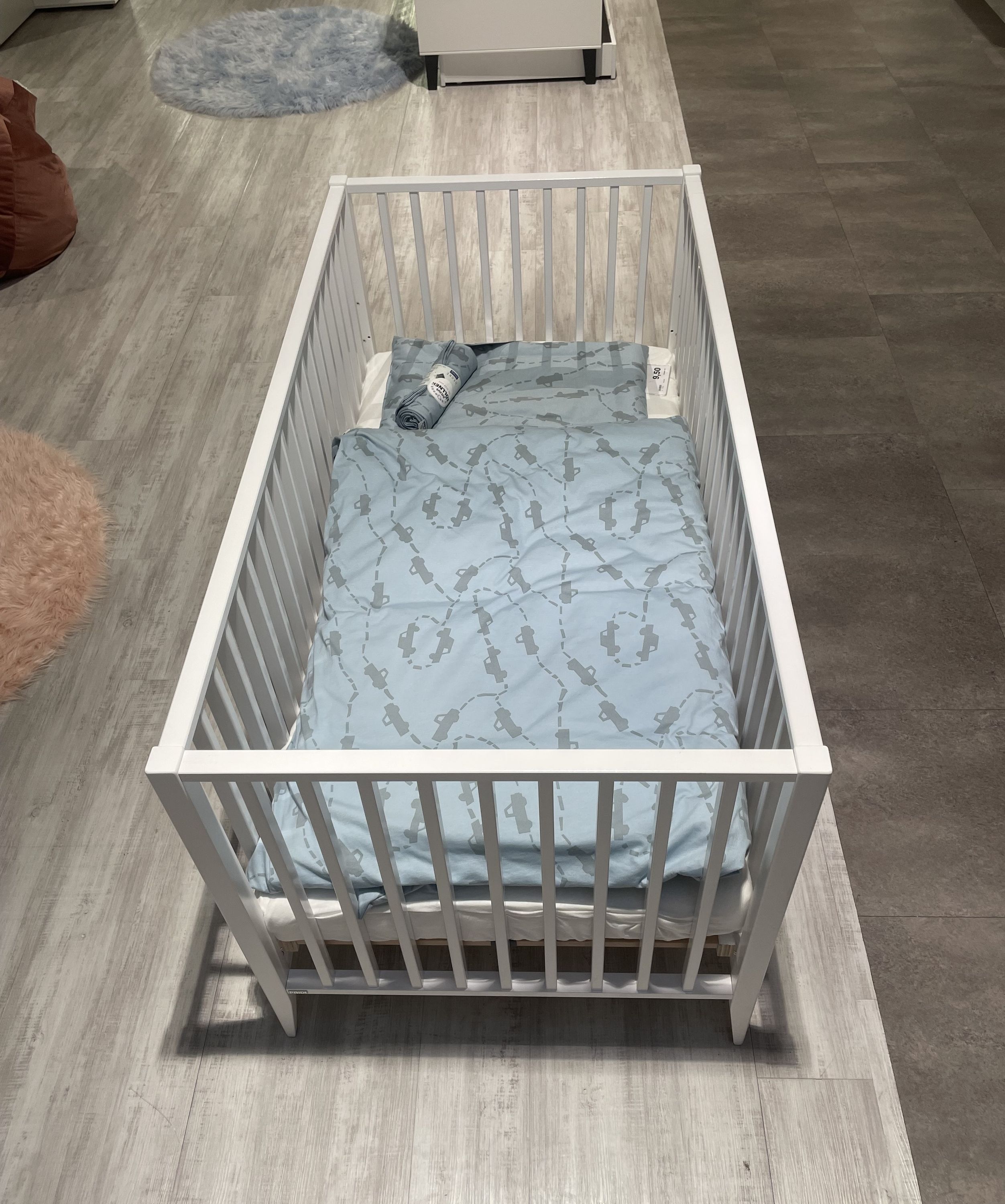 Weißes Babybett mit Gitterstäben und blauer Bettdecke mit Muster