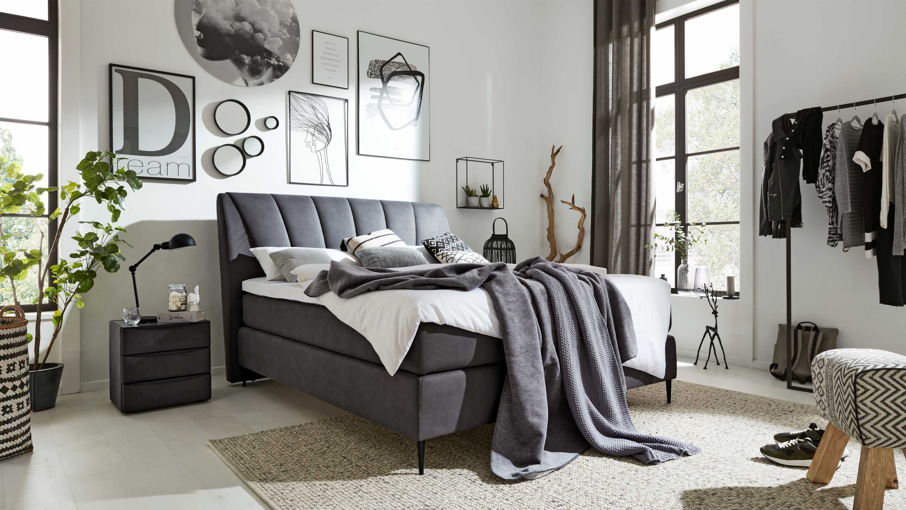 Anthrazitfarbenes Boxspringbett mit gepolstertem Kopfteil und schwarzen Beinen in modernem Schlafzimmer