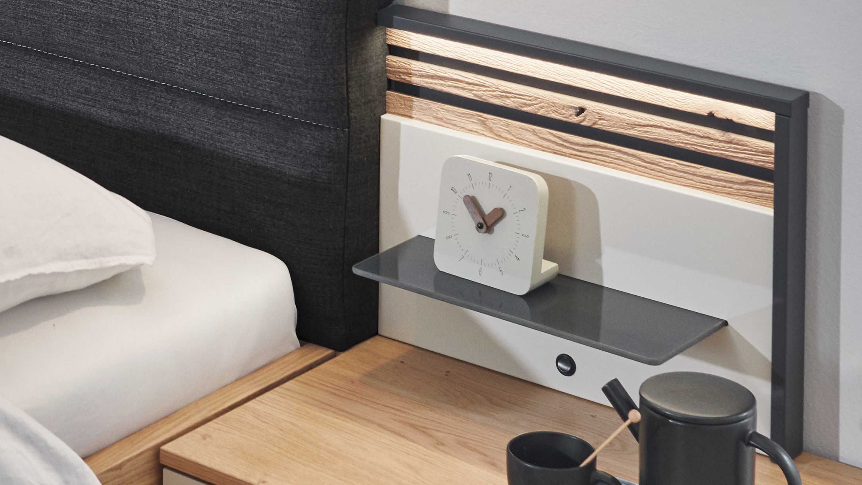 Rechteckiger Paneelaufsatz mit Holzoptik und grauem Regalbrett an Wand neben Bett