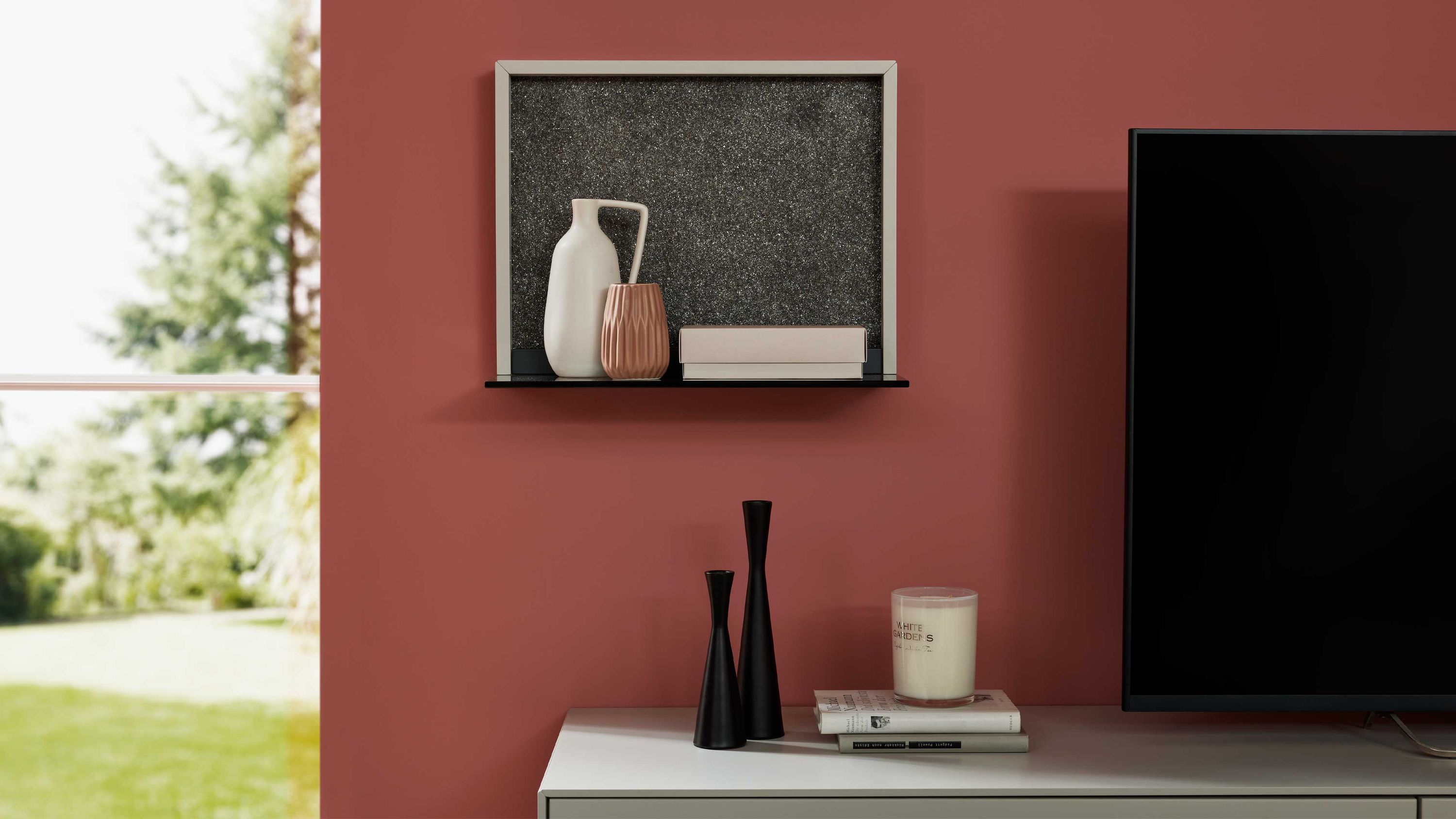 Wandboard mit schwarzer Ablagefläche und cremefarbenem Rahmen an roter Wand mit Dekoration