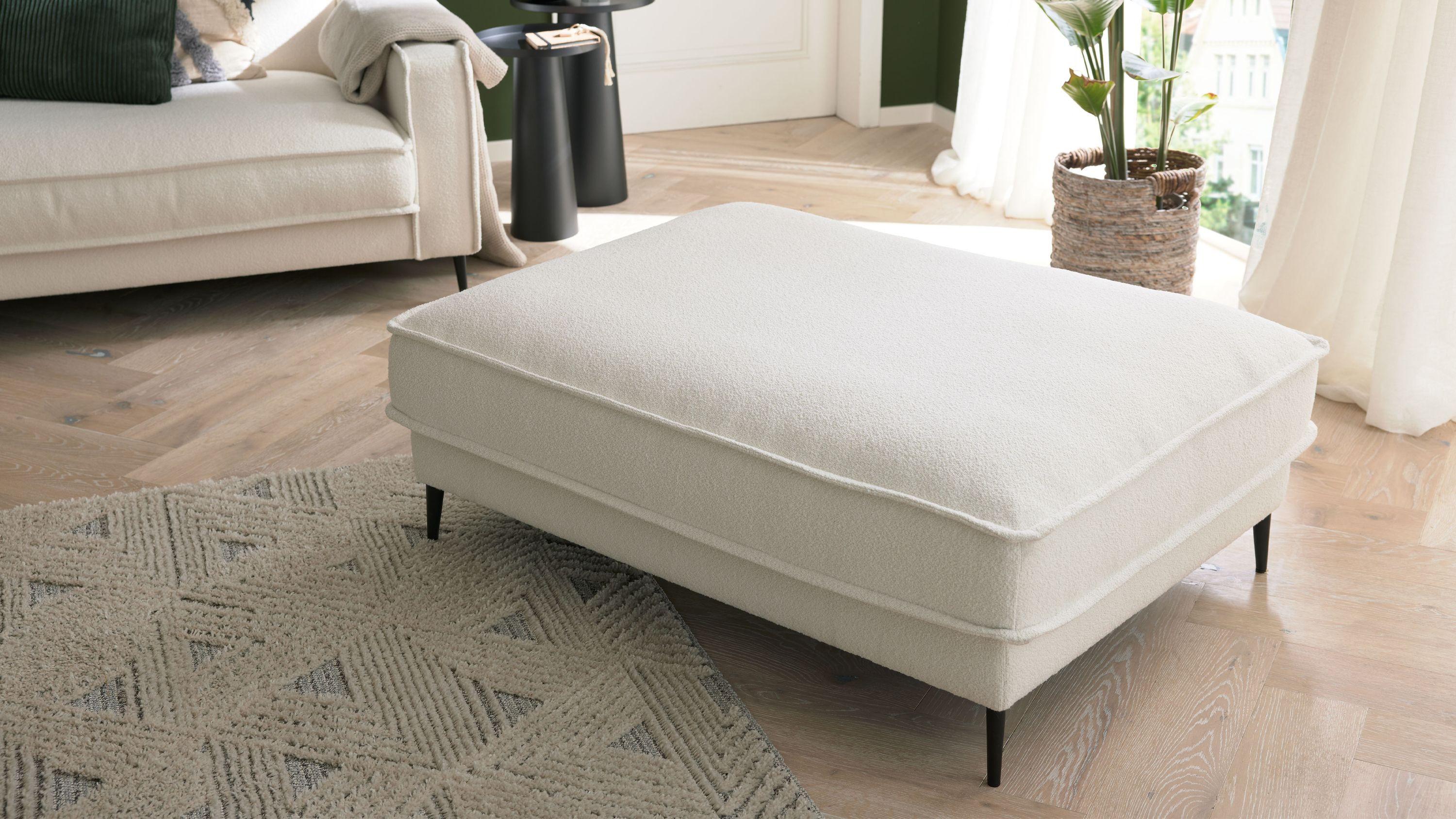 XXL-Polsterhocker mit weißem Stoffbezug und Metallfüßen Großer rechteckiger Polsterhocker mit weißem Stoffbezug und schlanken schwarzen Metallfüßen in einem Wohnzimmer