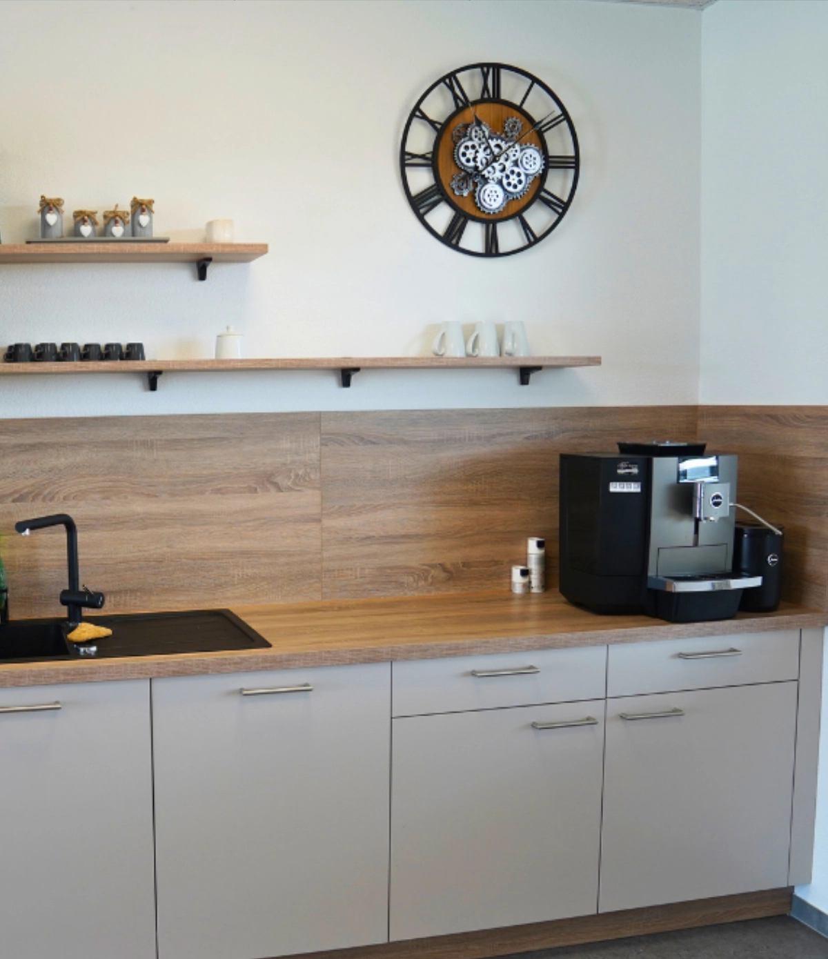 Moderne Büroküche mit Kaffeemaschine, Spüle, Holzarbeitsfläche, Hängeregalen und Wanduhr, funktionaler Pausenbereich im Office Design