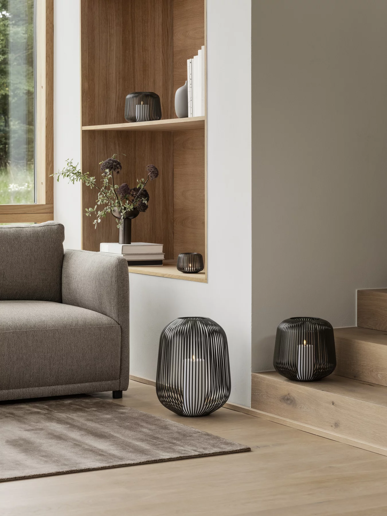 Zwei schwarze Windlichter eins am Boden neben Treppe eins im Wandregal  mit Sofa Holzboden & minimalistischer Einrichtung