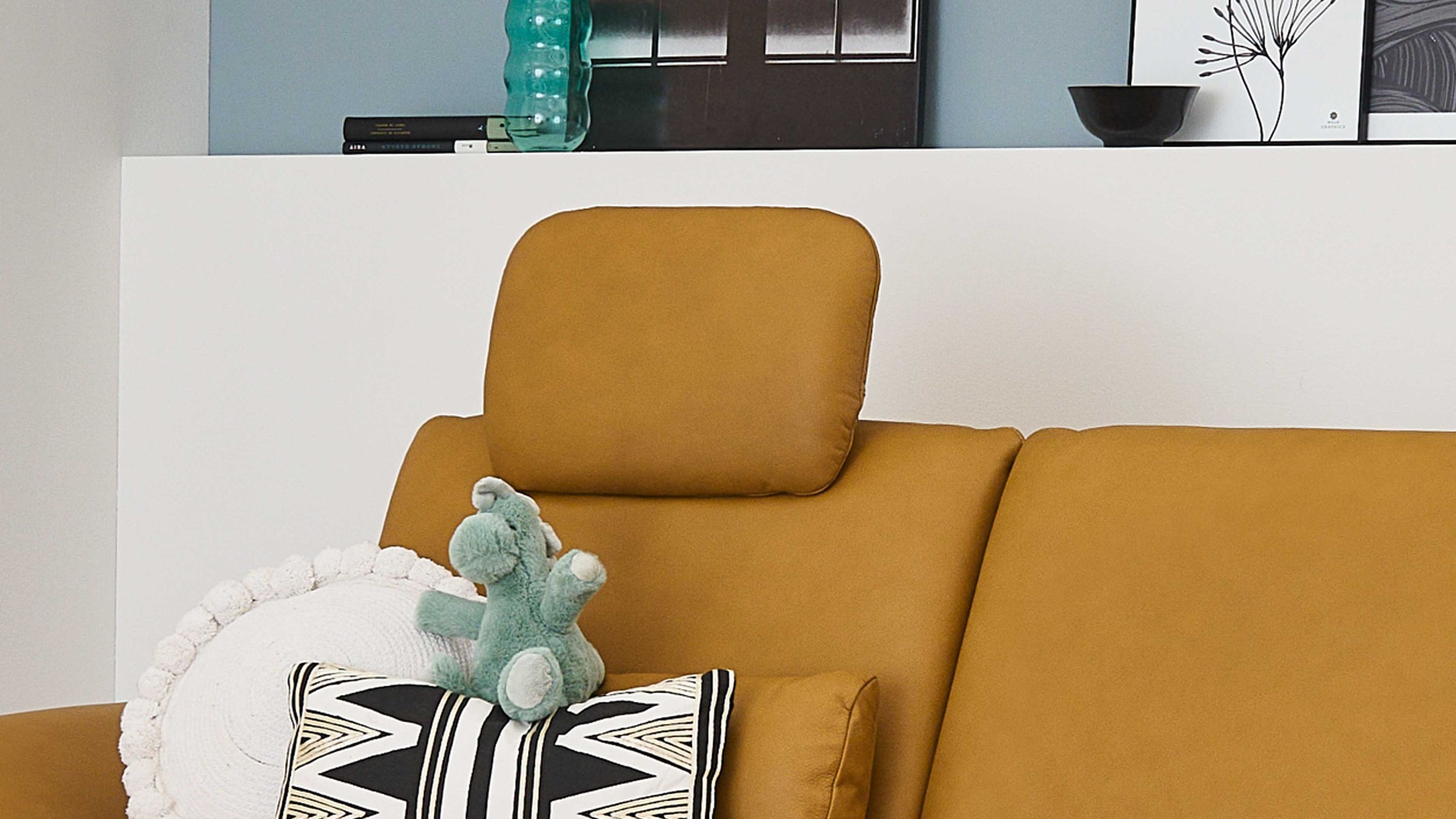 Sofa mit kurkumafarbenem Kopfstützenpolster und zwei Kissen in einem Wohnzimmer