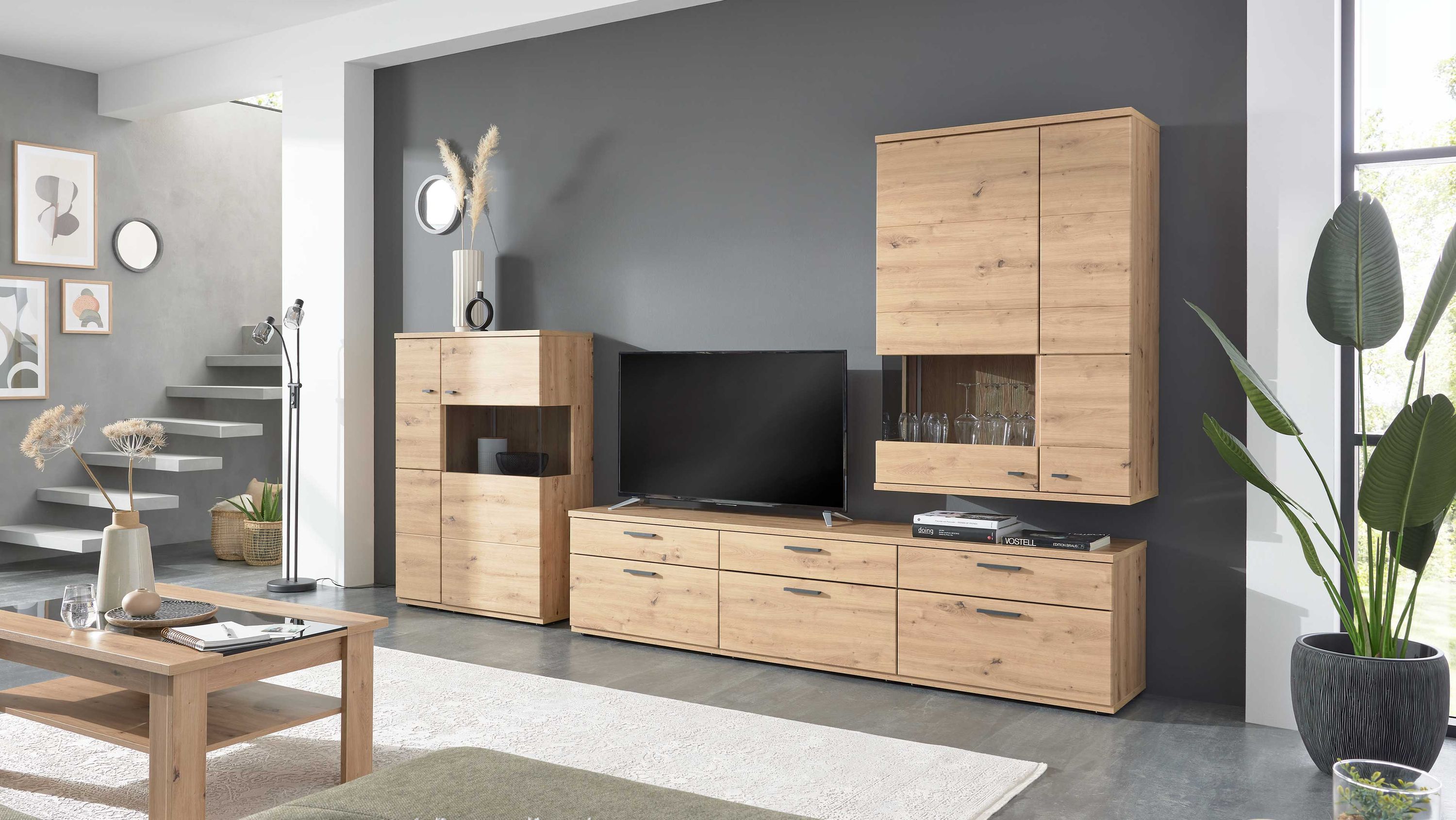 Fünfteilige Wohnwand aus hellem Holz mit TV-Board und Schränken Fünfteilige Wohnwand aus hellbraunem Holz mit Schränken Vitrinen und TV-Board vor dunkelgrauer Wand