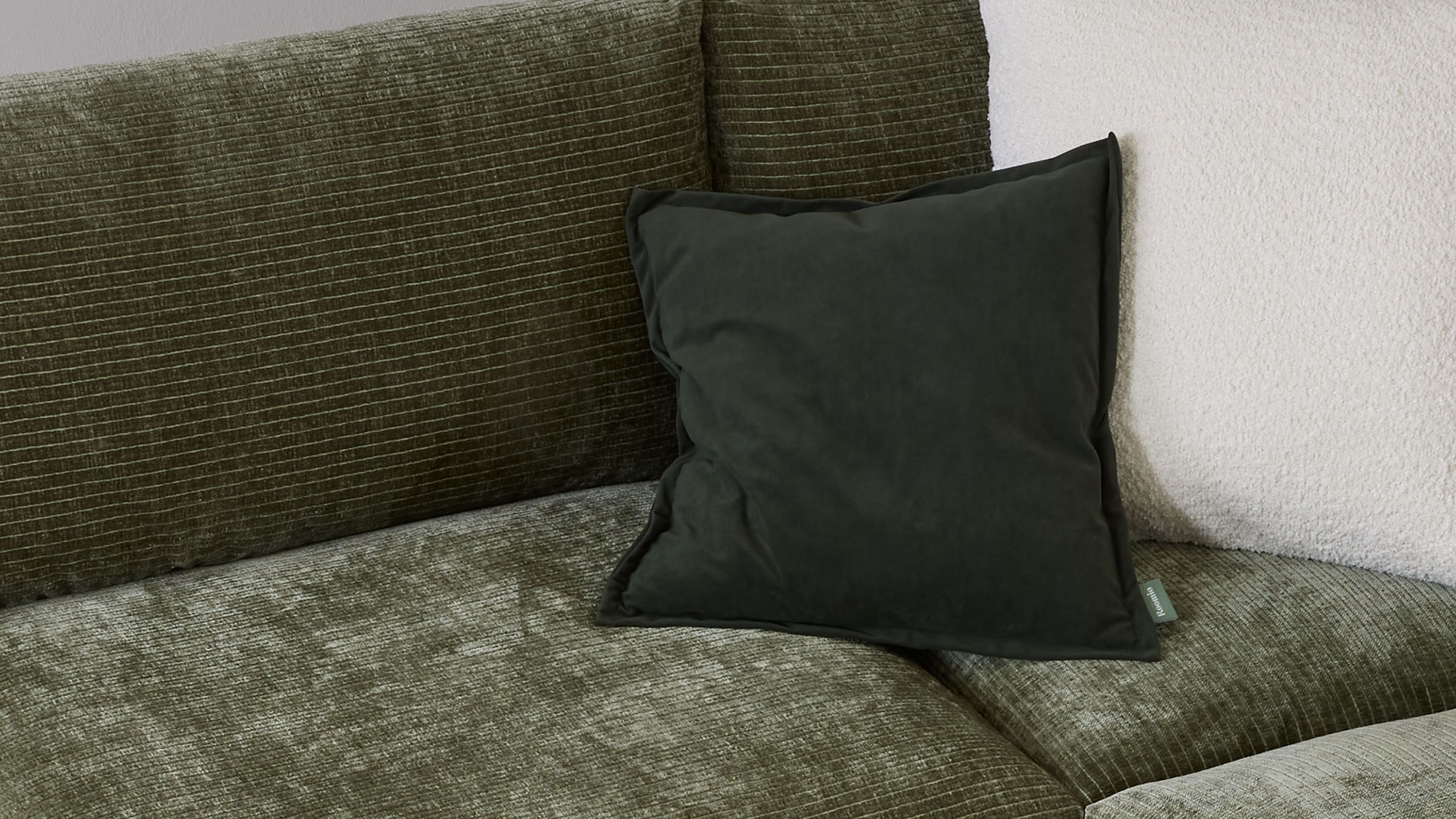 Quadratisches Kissen in dunklem Grün auf grünem Sofa mit Struktur