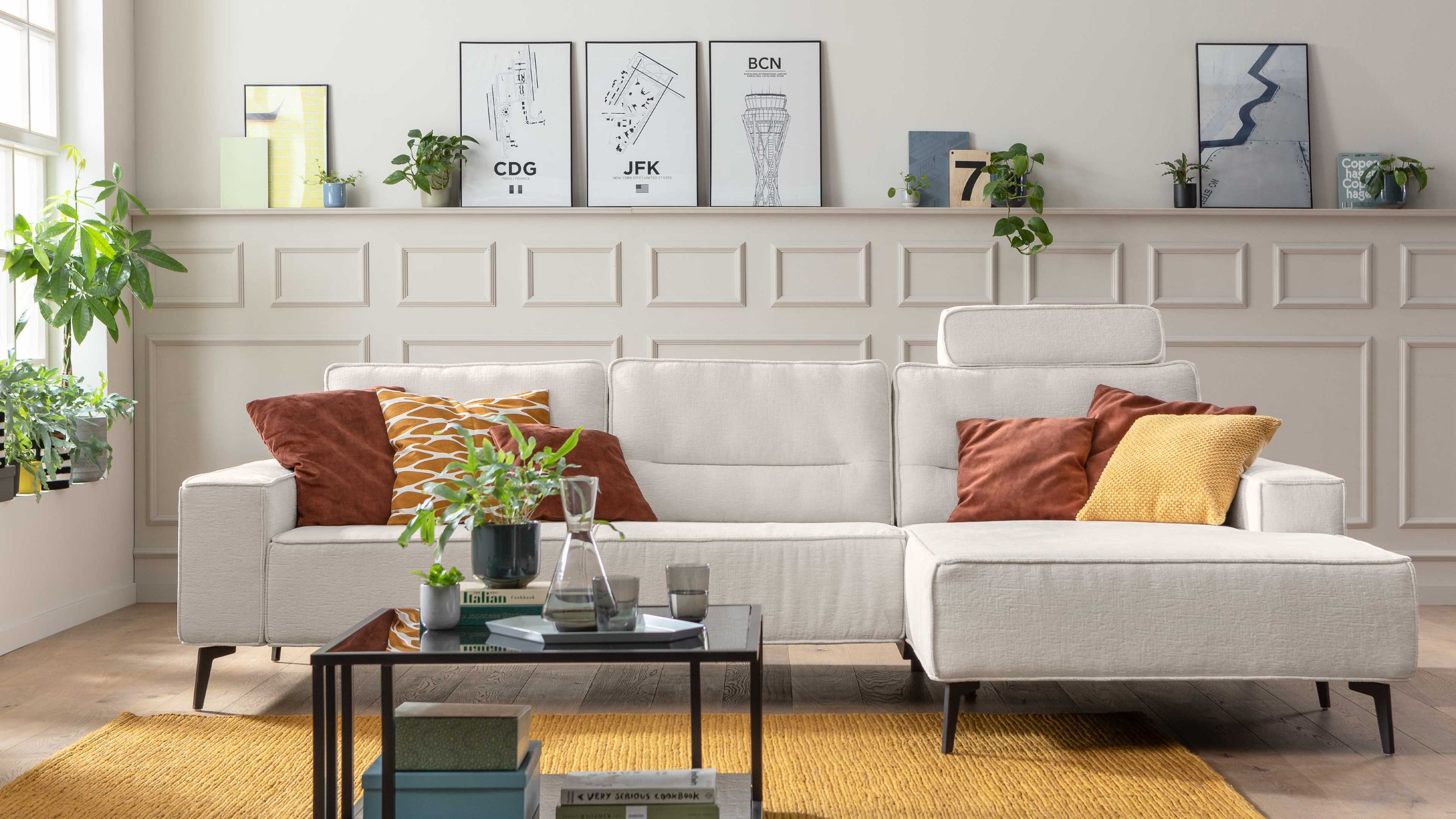 Ecksofa mit naturweißem Stoffbezug schwarzen Metallfüßen bunten Kissen schwarzer Couchtisch auf gelbem Teppich