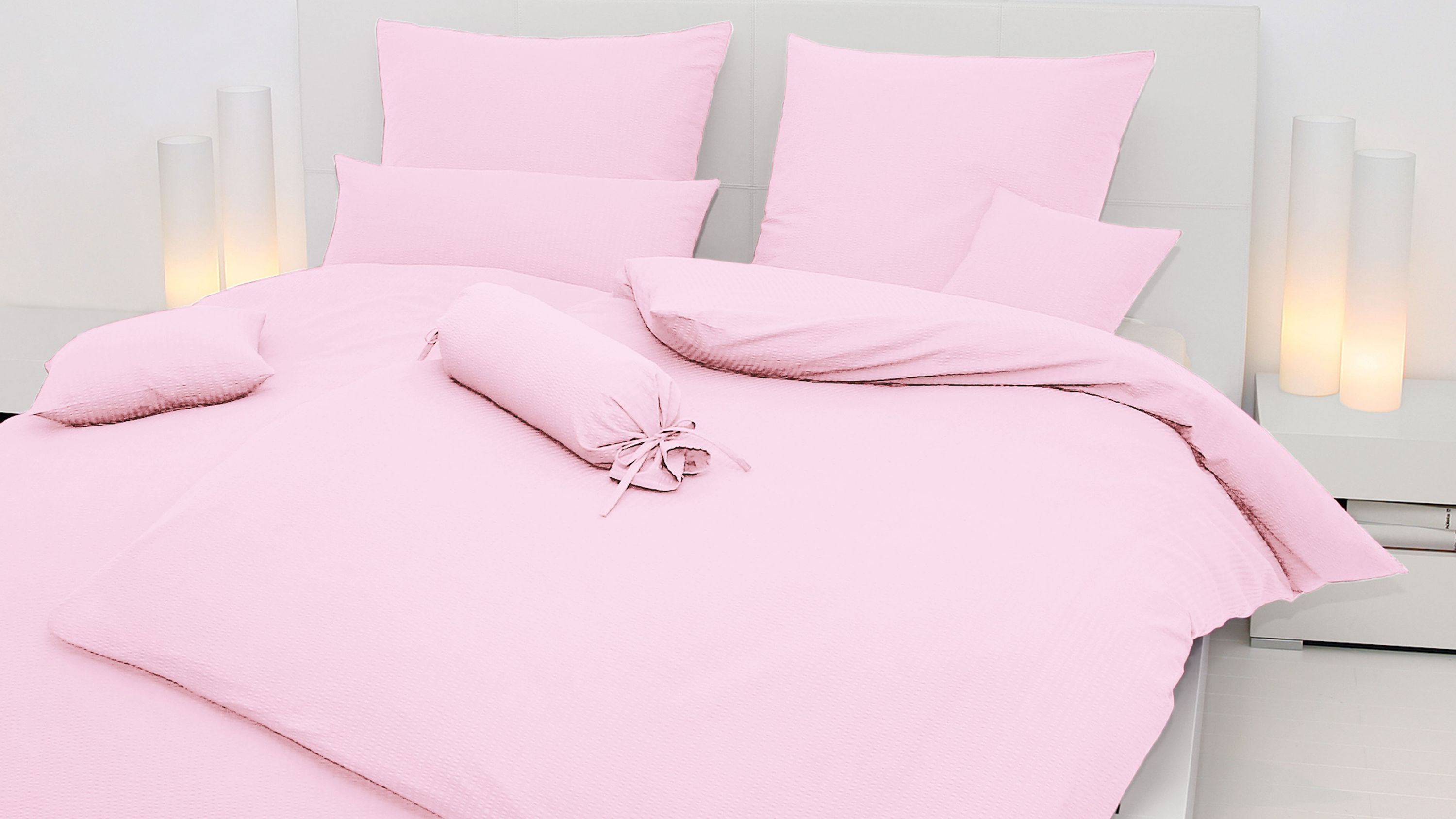 Bett mit zartrosa Bettwäsche bestehend aus Kissen und Decke auf weißem Kopfteil