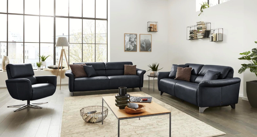 Helles Wohnzimmer mit schwarzem Ledersofa-Set, Sessel, Couchtisch und großen Fenstern im modernen Loftstil.