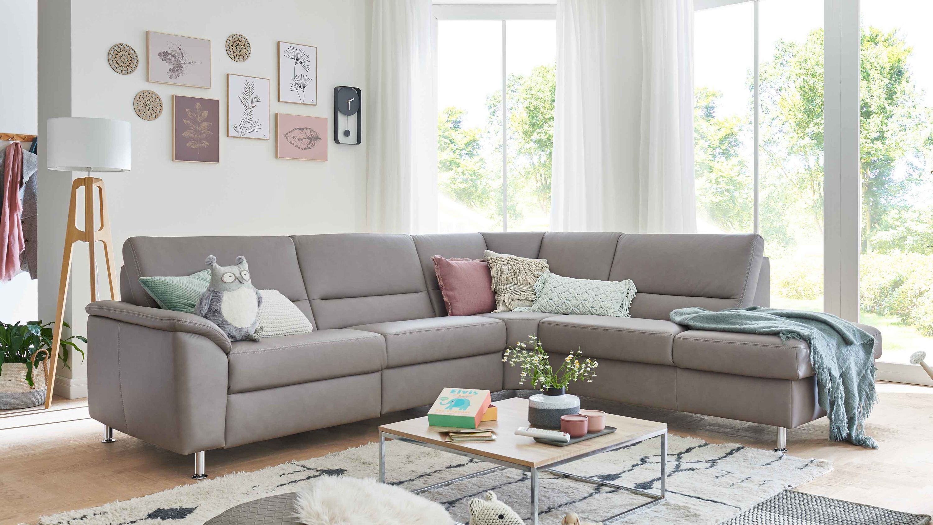 Ecksofa mit granitfarbenem Lederbezug und Alufüßen dekoriert mit Kissen und Decke in hellem Wohnzimmer