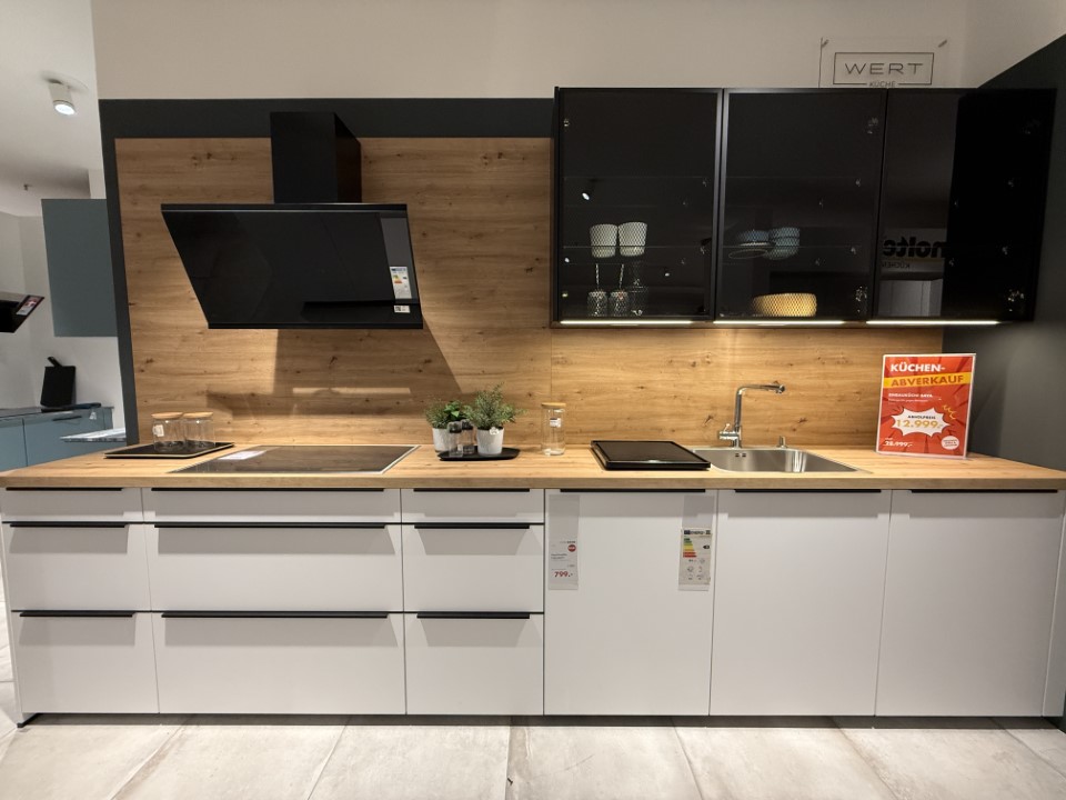 Moderne Küchenzeile mit weißen Unterschränken, Holzarbeitsplatte und schwarzem Glasoberschrank