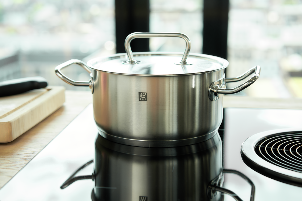 Edelstahl-Kochtopf mit Deckel und seitlichen Griffen auf Induktionskochfeld in moderner Küche
