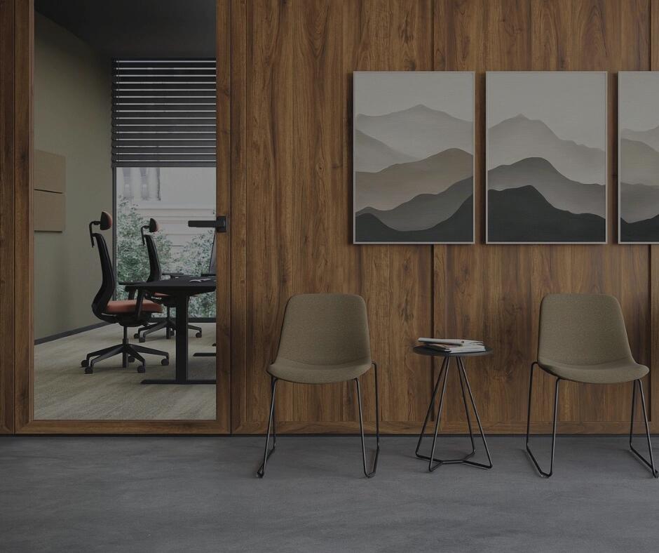 Moderner Wartebereich mit Holzverkleidung, zwei Stühlen, Beistelltisch, Landschaftsbildern und Blick in ein Büro durch Glastür.