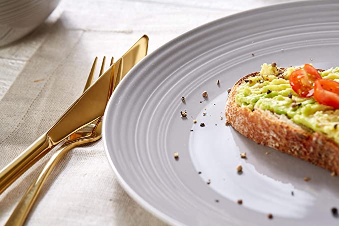 Avocado-Toast mit Stil – Frühstück in Nahaufnahme Nahaufnahme: Avocado-Toast mit Tomaten und Pfeffer auf Teller, goldenes Besteck auf Leinentuch daneben.