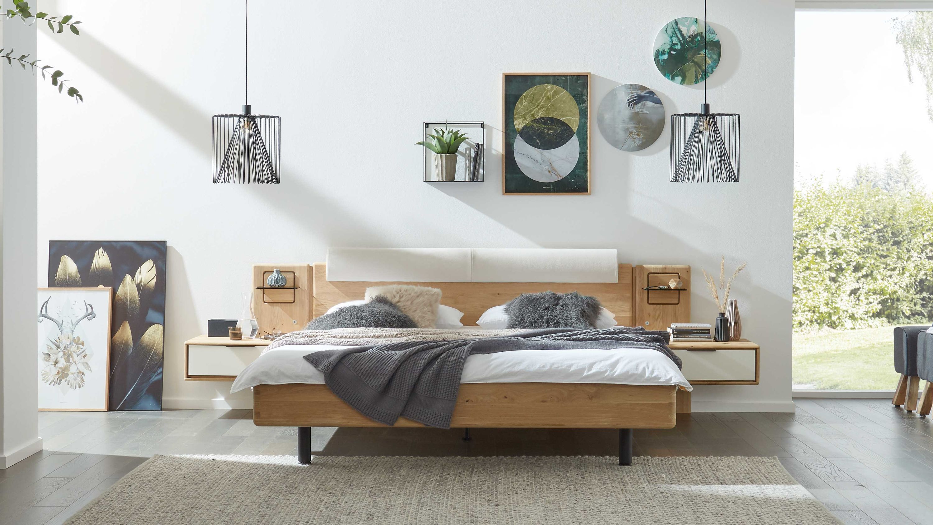 Bettgestell mit cremefarbenem Bezug und Holzrahmen in hellem Braun mit zwei Nachttischen an der Wand