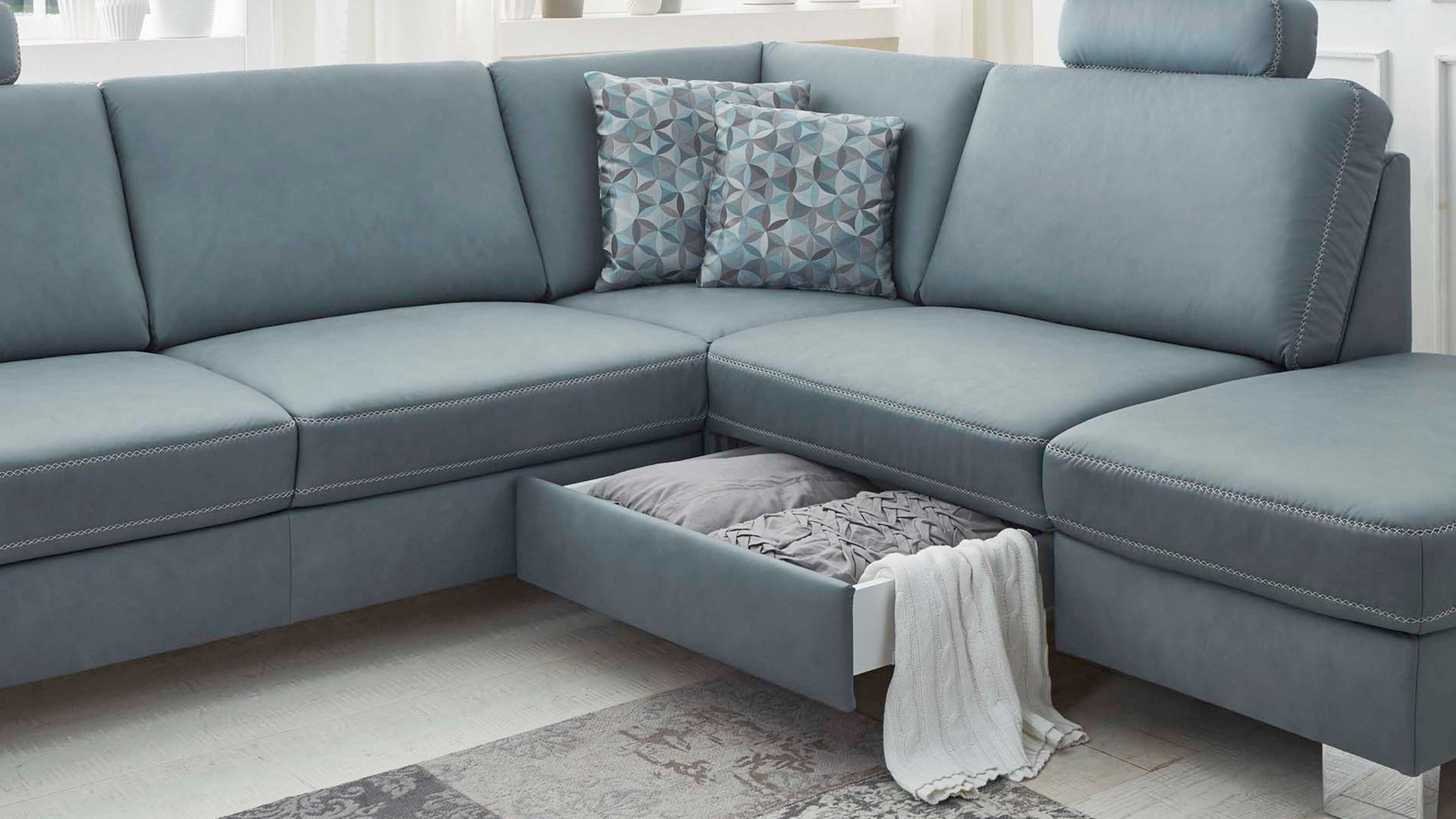 Ecksofa mit hellblauem Bezug und offener Schublade unter der Sitzfläche mit Decken und Kissen