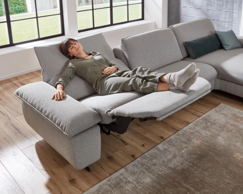 Relaxsofa von Himolla mit Komfortfunktion Mann entspannt auf grauem Sofa mit ausklappbarer Fußstütze in hellem Wohnzimmer